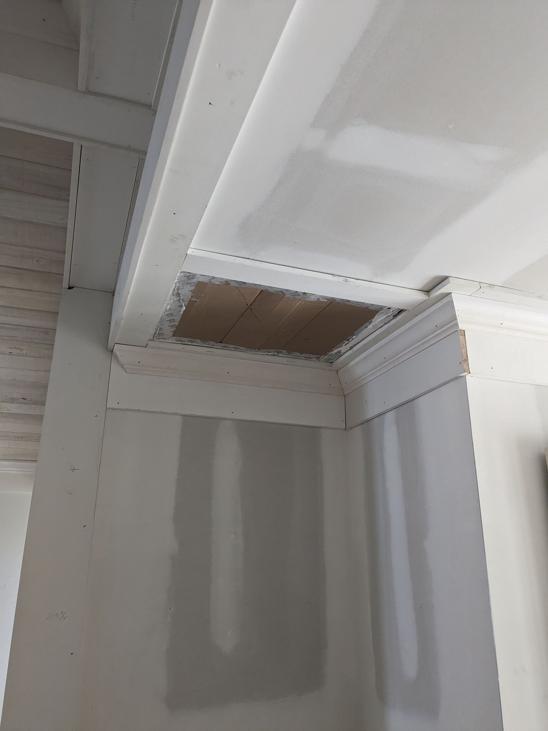 An unfinished drywall corner showing a hole in the ceiling, exposed wooden framing, and installed metal corner beads.