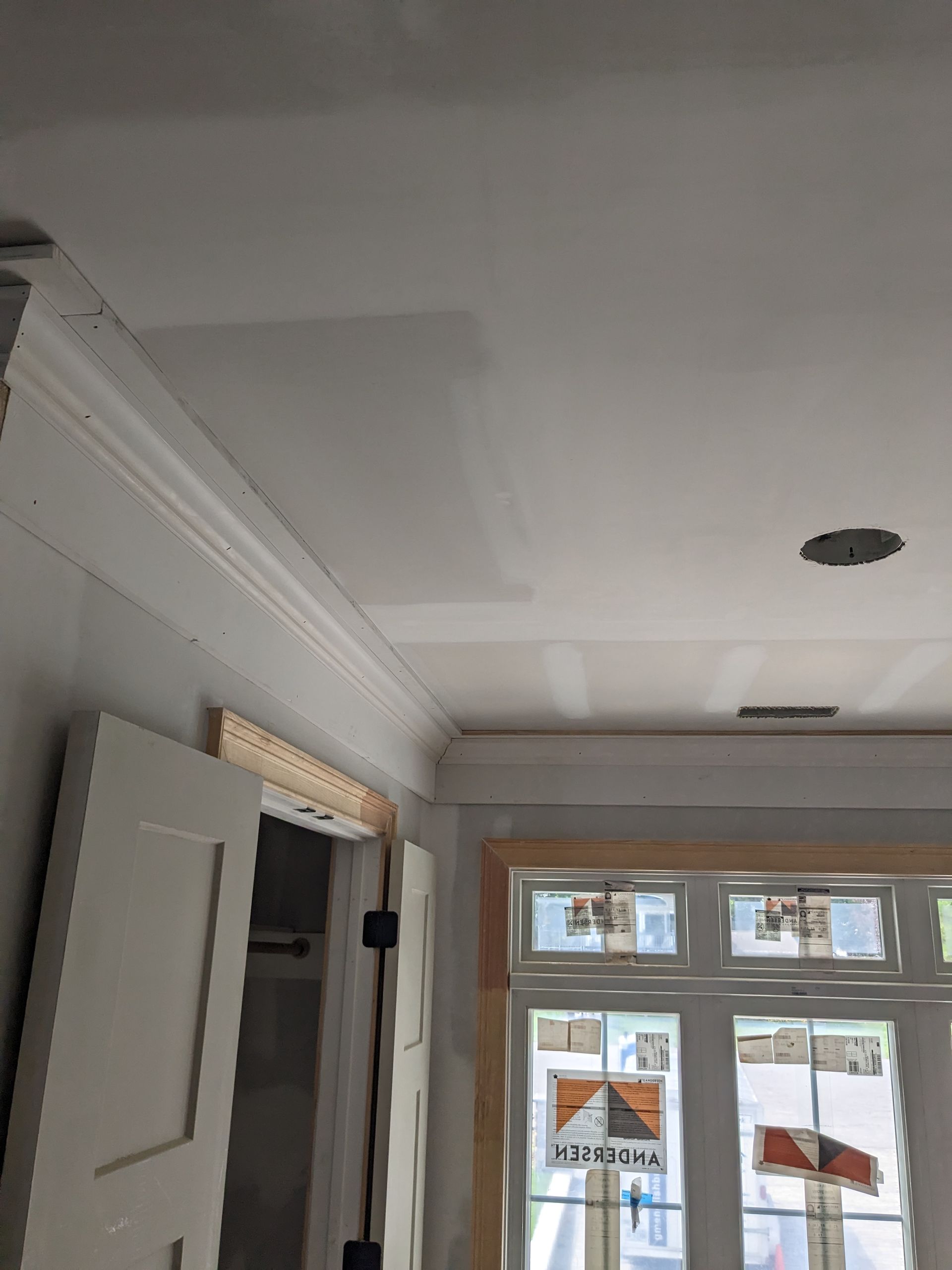 Unfinished interior room with white drywall, crown molding, and bare wood trim around a door and window.