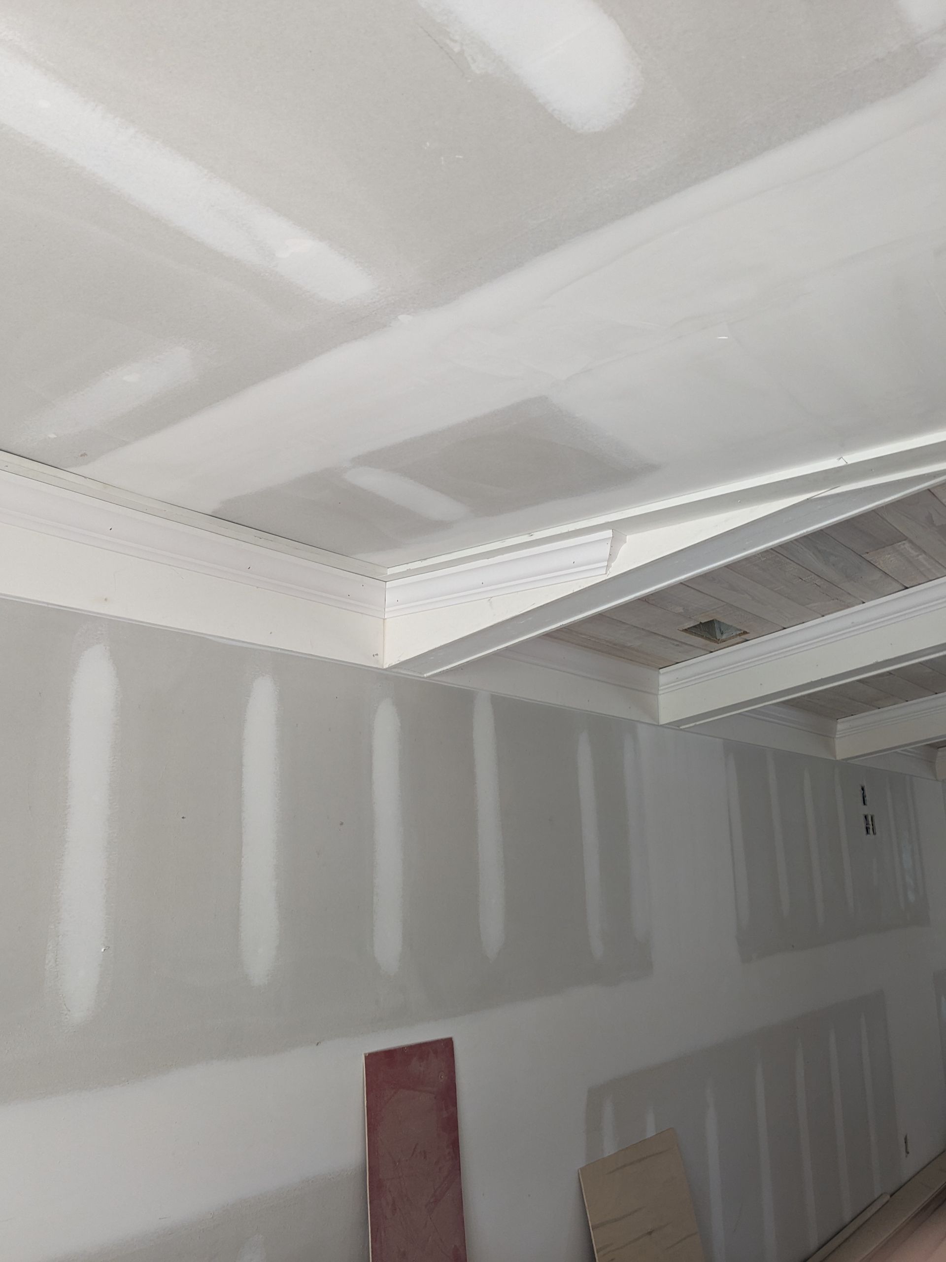 An interior shot of a room under construction, showing white drywall with taped seams and white crown molding on the ceiling.
