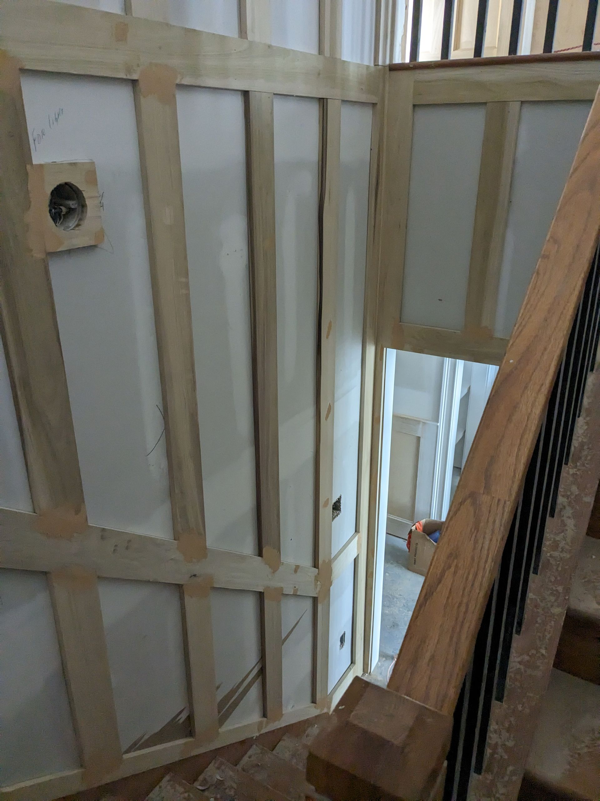 A staircase with a wood railing alongside a wall featuring decorative vertical and horizontal wood molding trim.