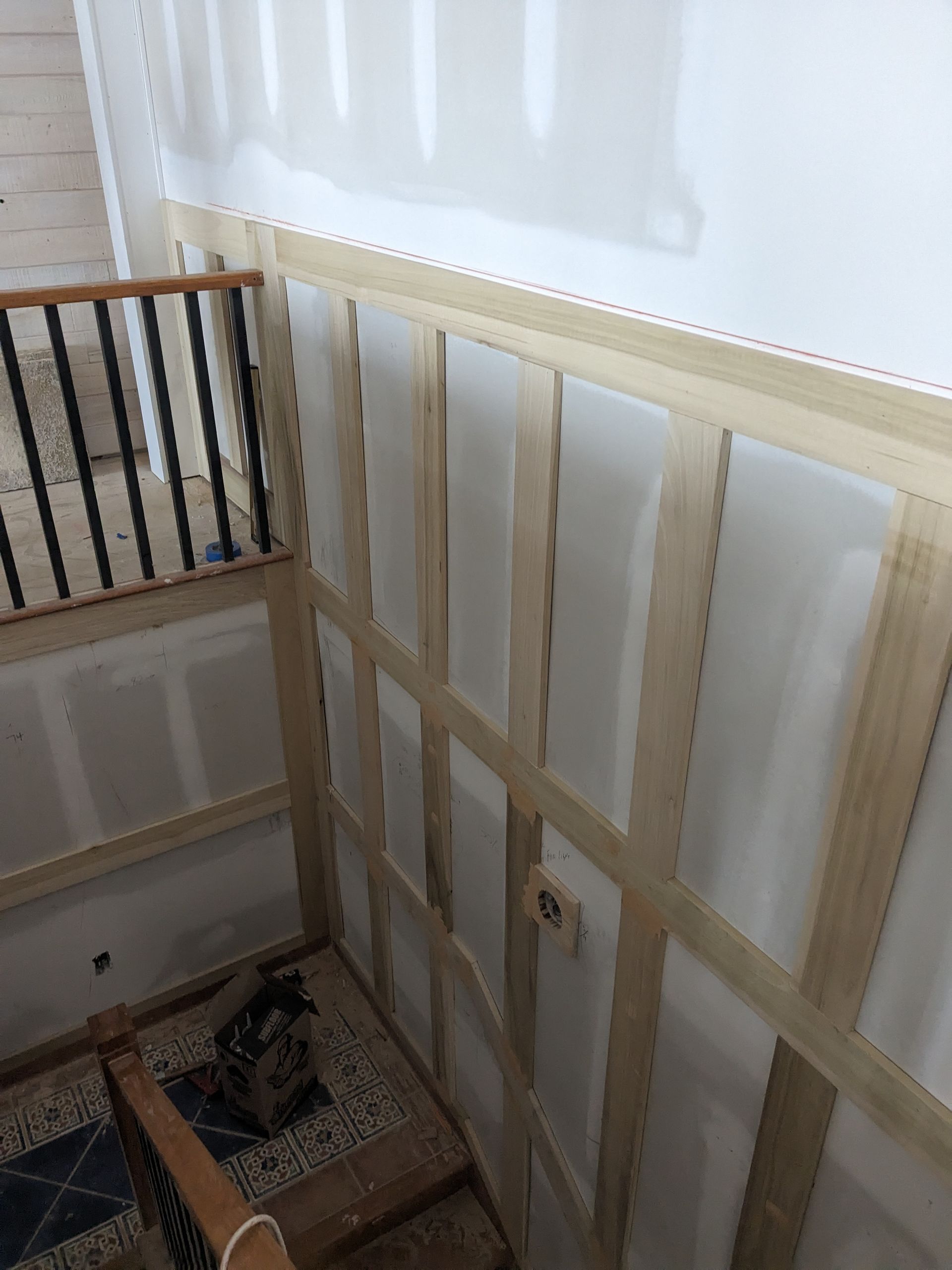 A wooden wainscoting frame installed on a staircase wall with drywall patches and metal stair railing.