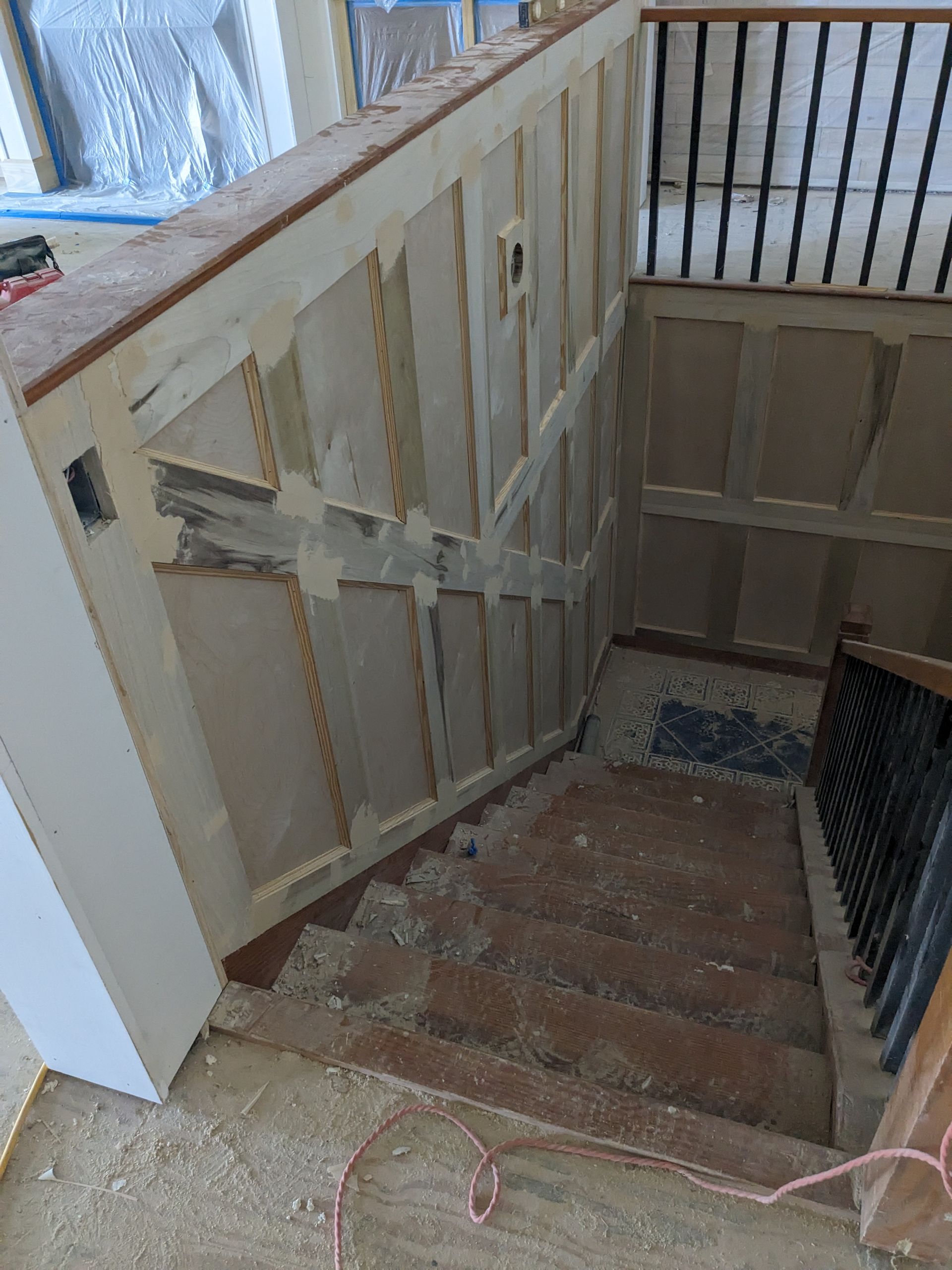 A staircase under construction with partially installed wood paneling on the side walls and a metal railing.