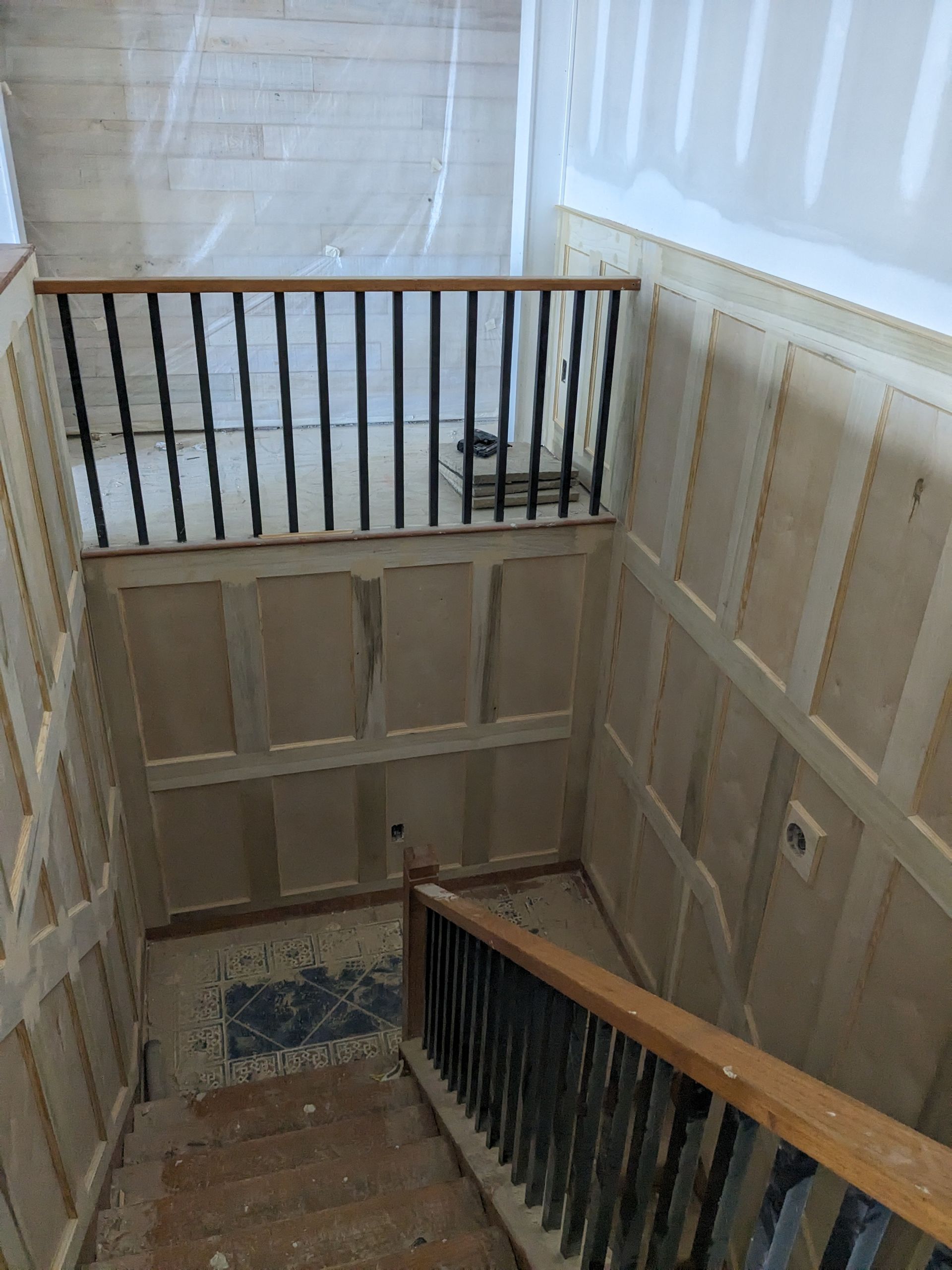 Staircase with light-colored wainscoting and wooden railings, currently under renovation with unfinished wall panels.