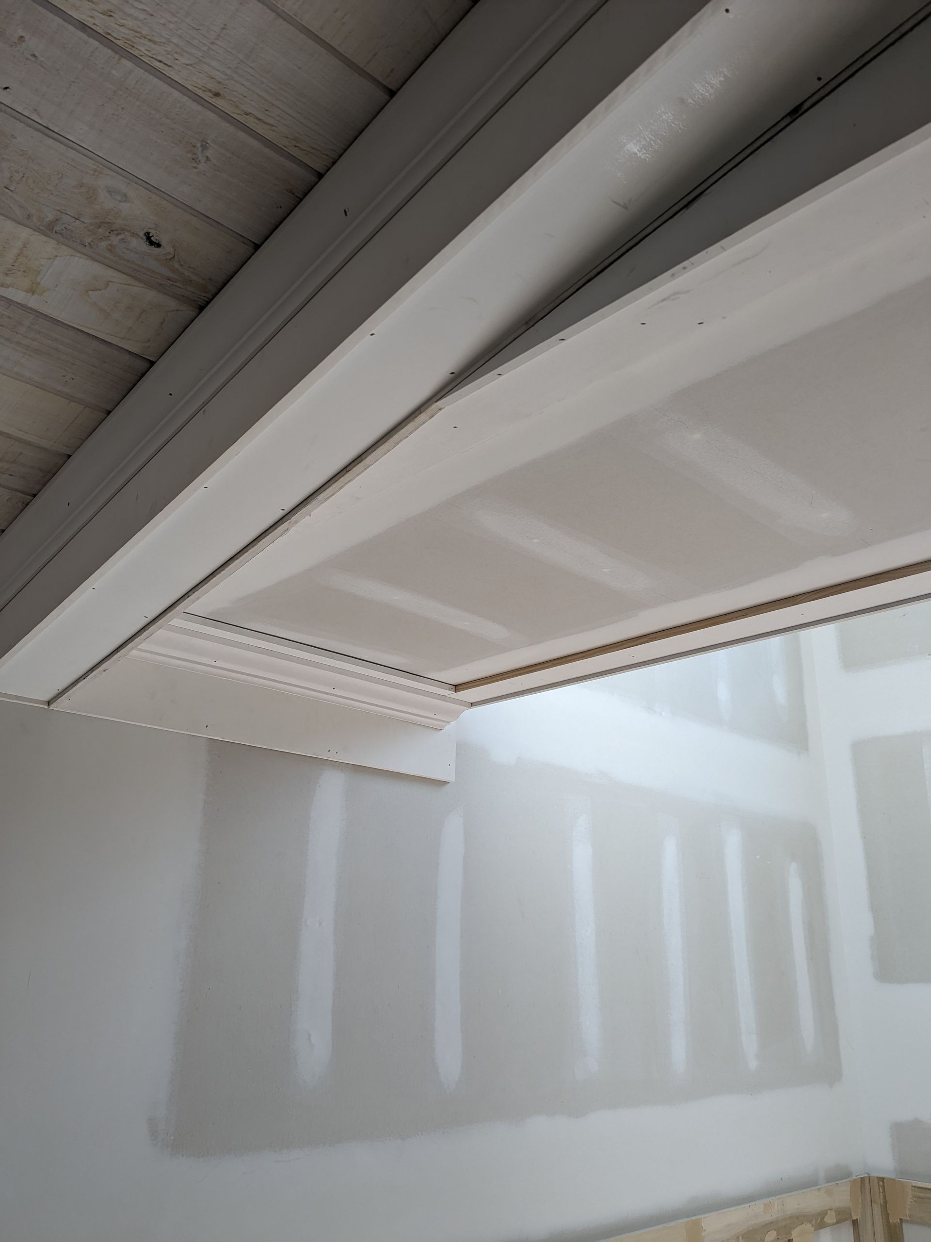 Drywall construction showing a finished ceiling soffit with corner bead installed, adjacent to bare wall panels.