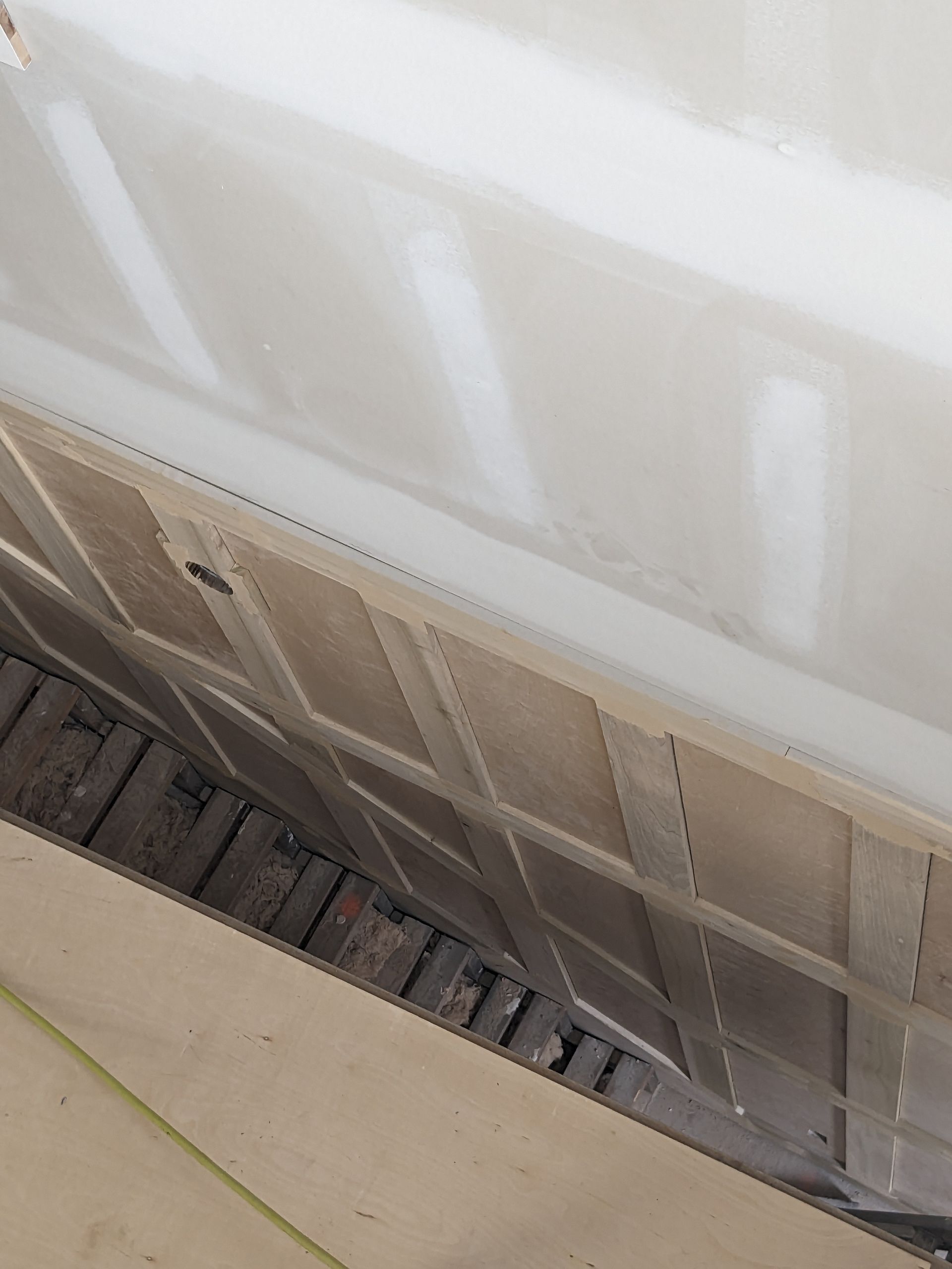 A close-up view of a white wall section with a visible gap above a brown wooden baseboard against a brick-lined floor.