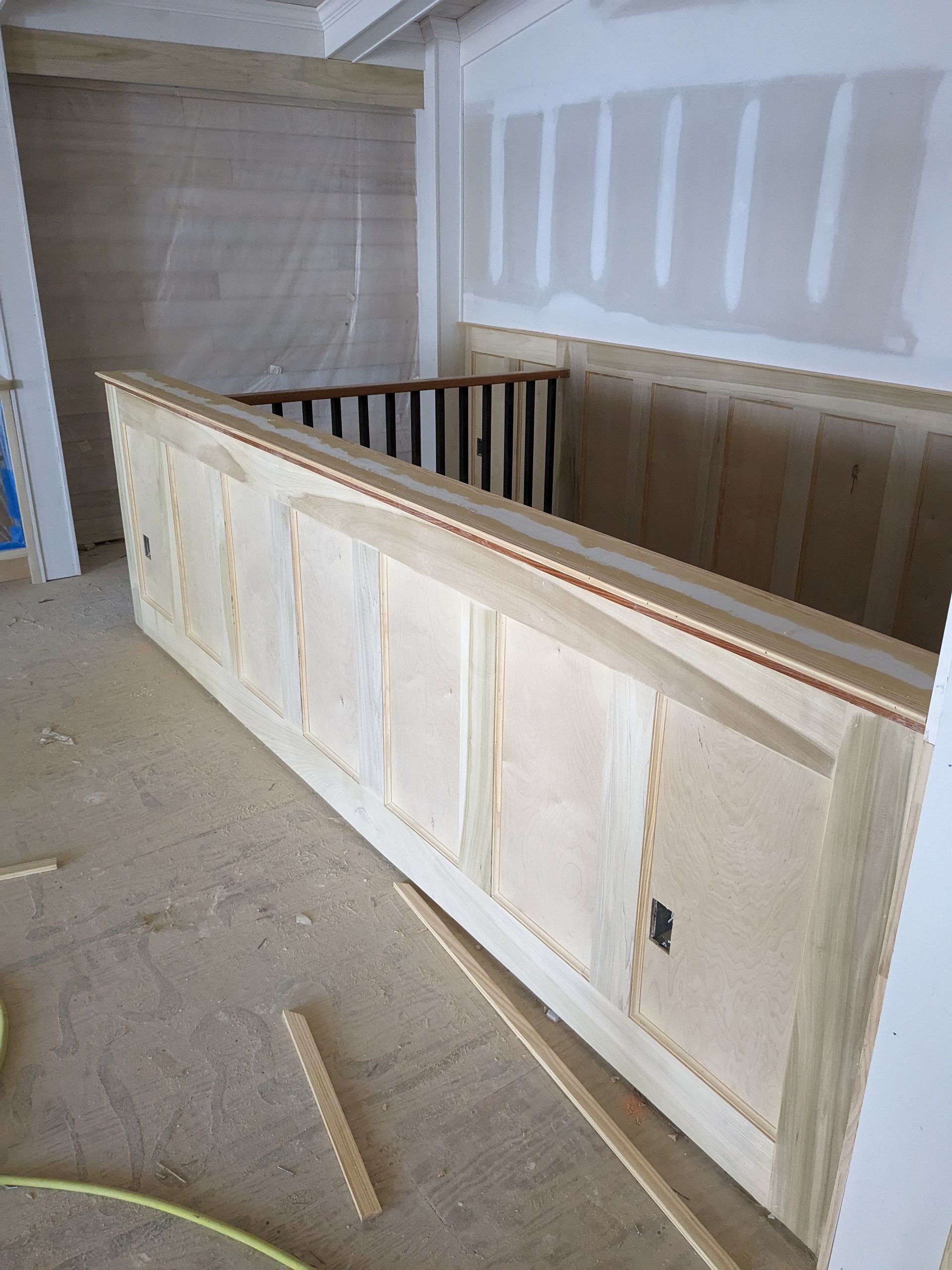 Unfinished wood wainscoting installed on a staircase wall in a room under construction with exposed drywall.