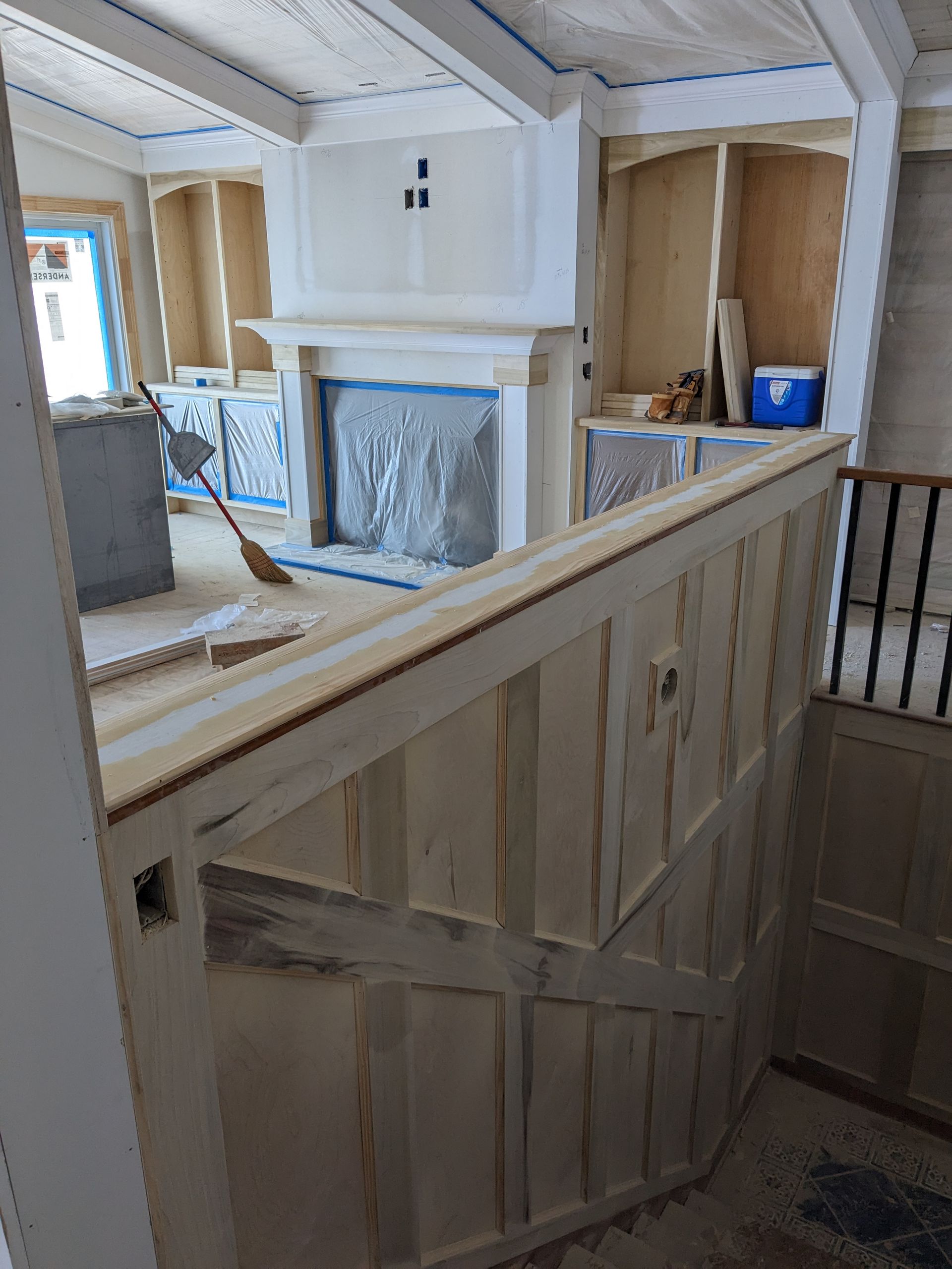 An interior view of a room under construction, featuring a staircase railing with decorative trim and a fireplace.
