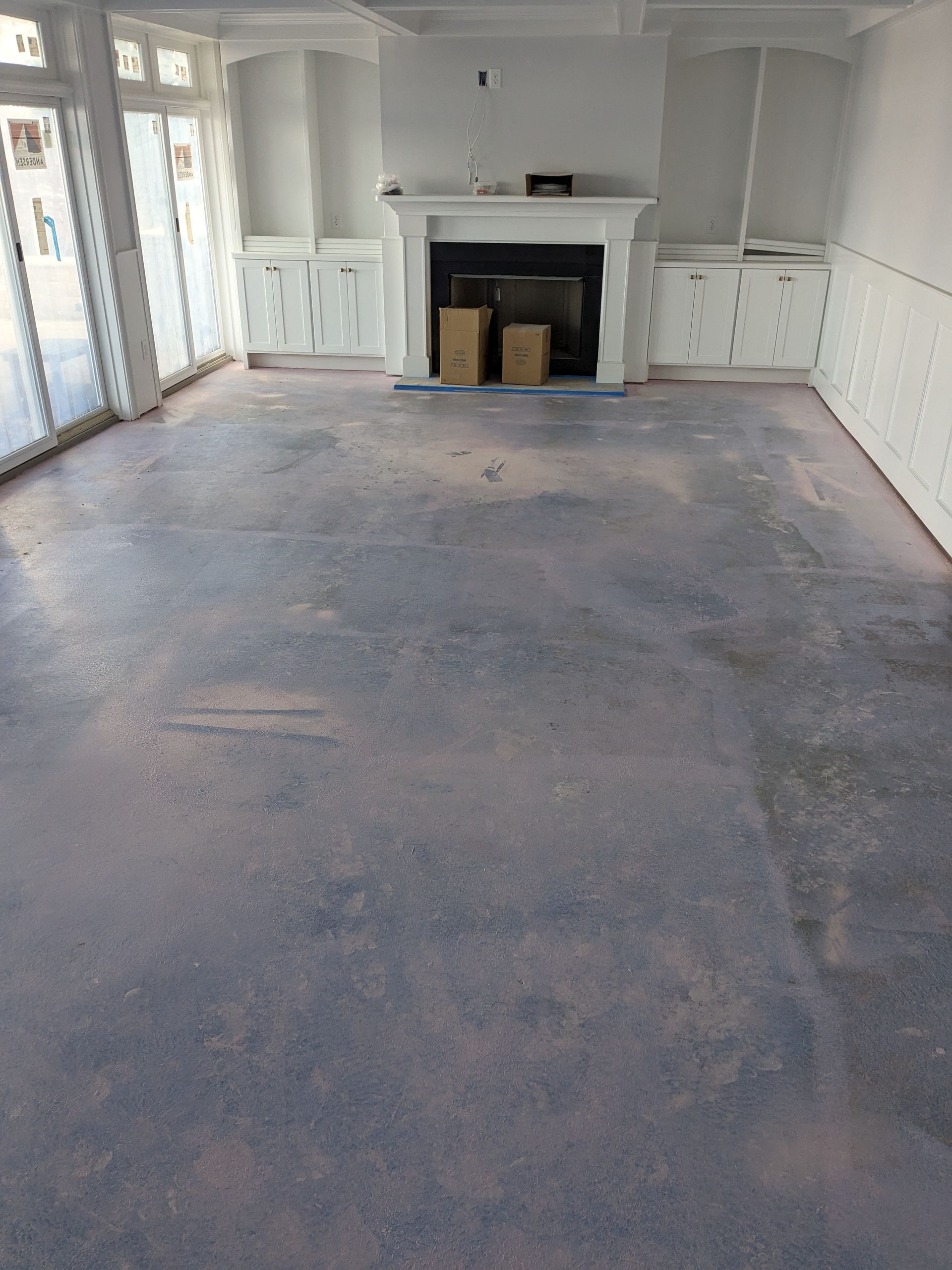A sparsely furnished room with a white fireplace, built-in shelving, glass doors, and a bare concrete subfloor.