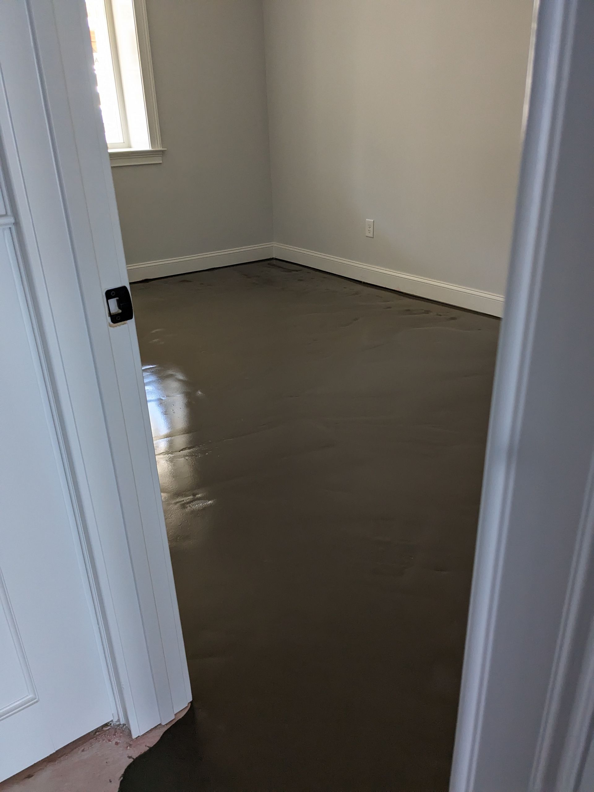A room with freshly applied, smooth gray concrete flooring visible through an open white doorway.