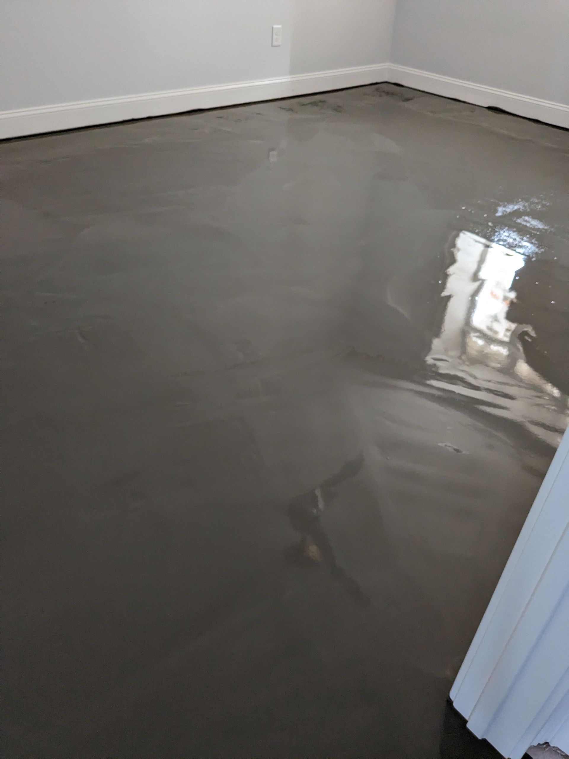 A freshly poured grey self-leveling floor compound covering a residential room floor, showing a reflective, smooth surface.