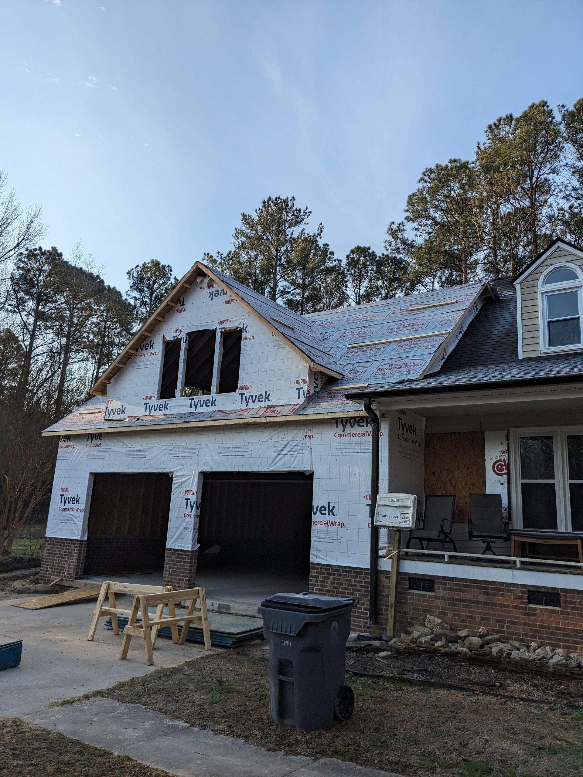 A house under construction with white exterior sheathing, two open garage bays, and brick accents on the lower level.