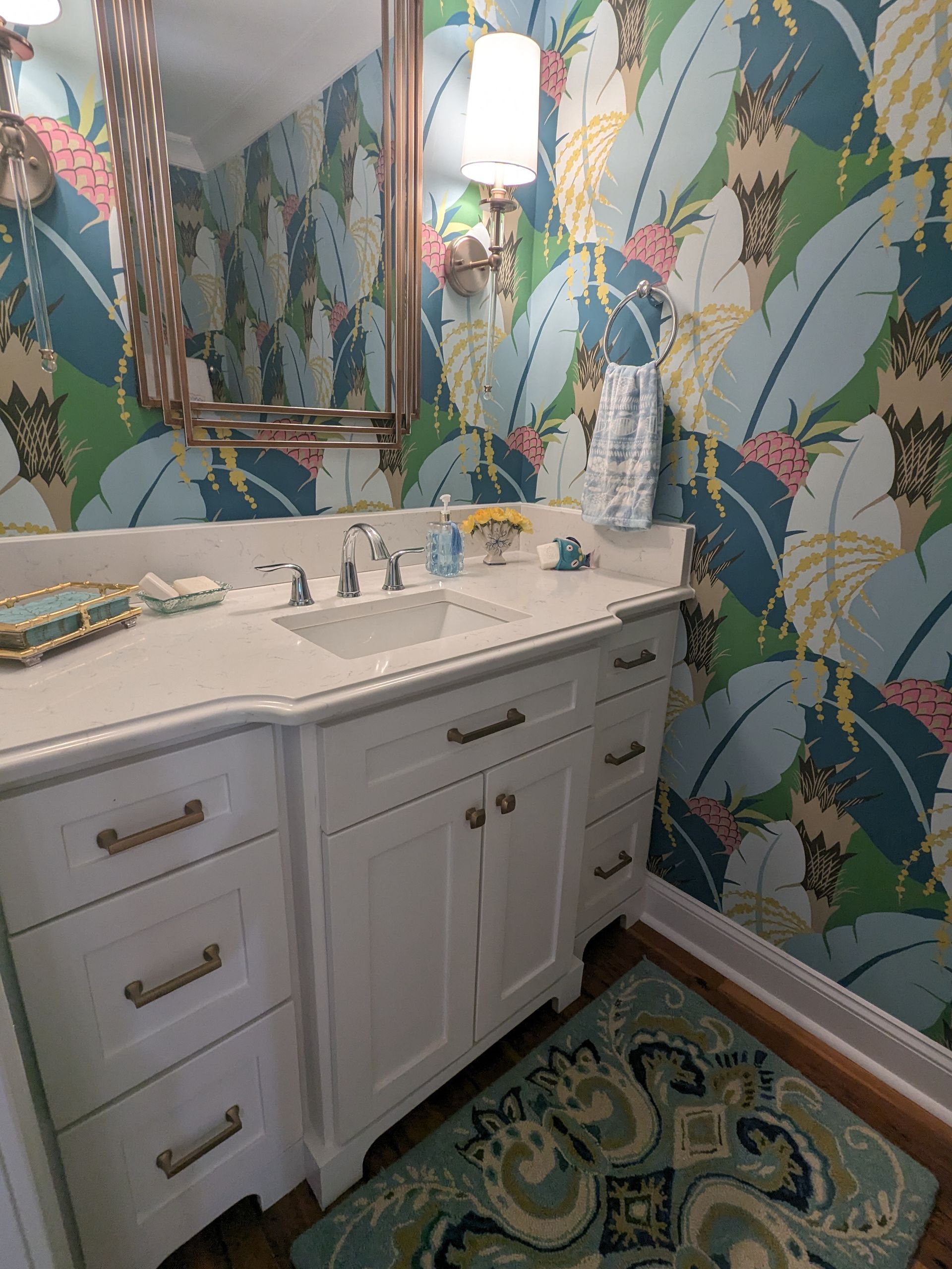 A bathroom vanity with a white cabinet, marble countertop, large mirror, and colorful tropical leaf wallpaper.