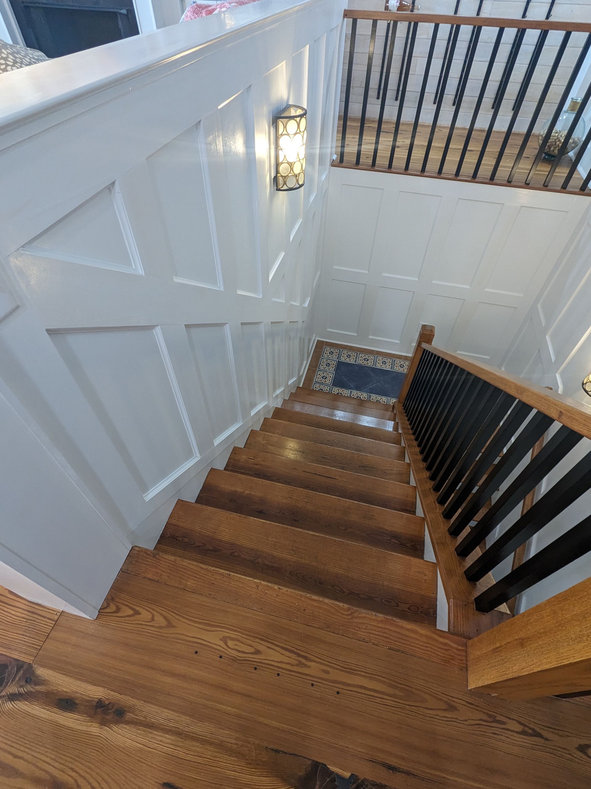 A high-angle view looking down a wooden staircase with white paneling and a dark railing leading to a lower level.