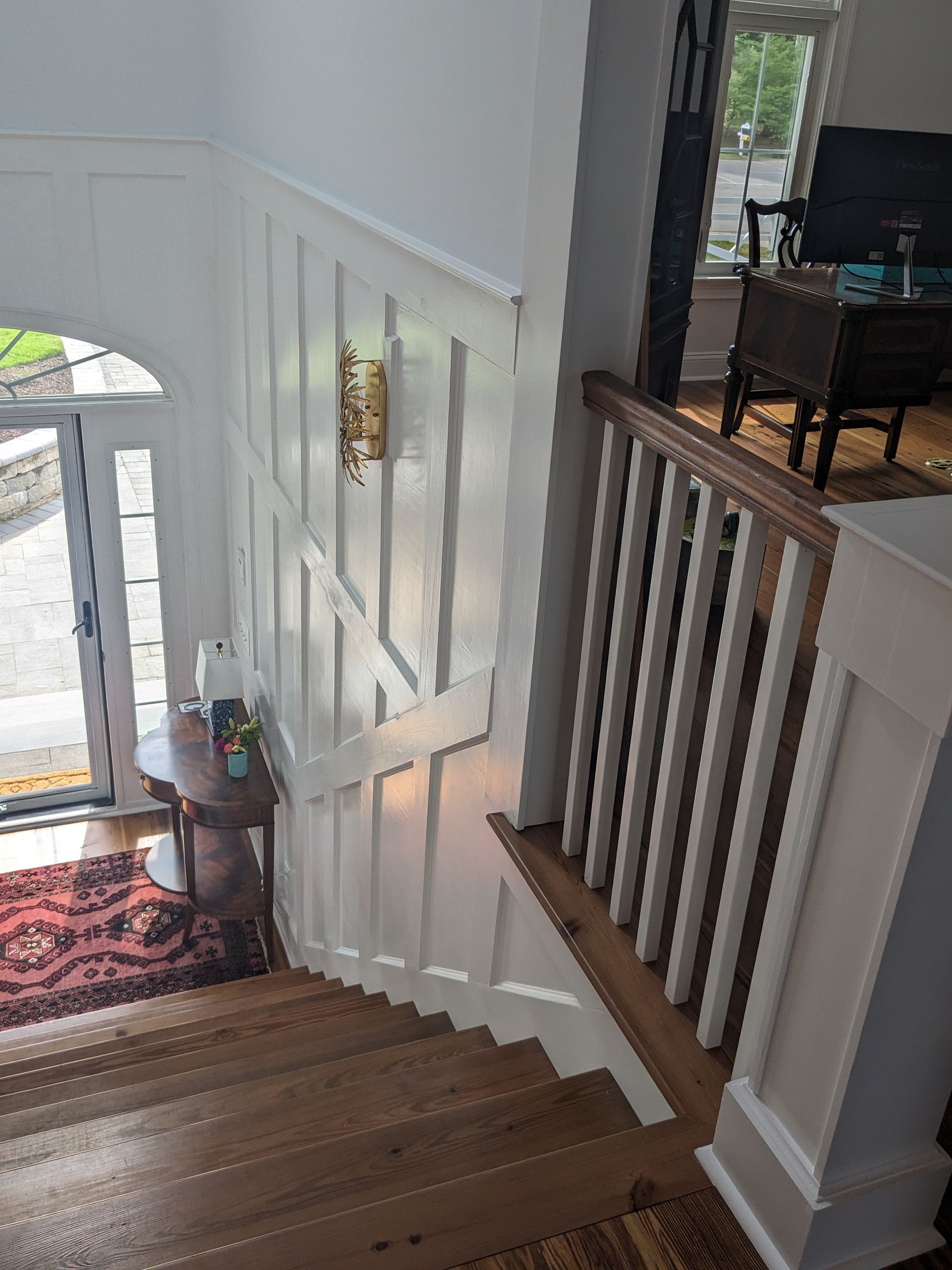 A view from the top of a wooden staircase looking down at a white board-and-batten wall and a doorway with a side table.