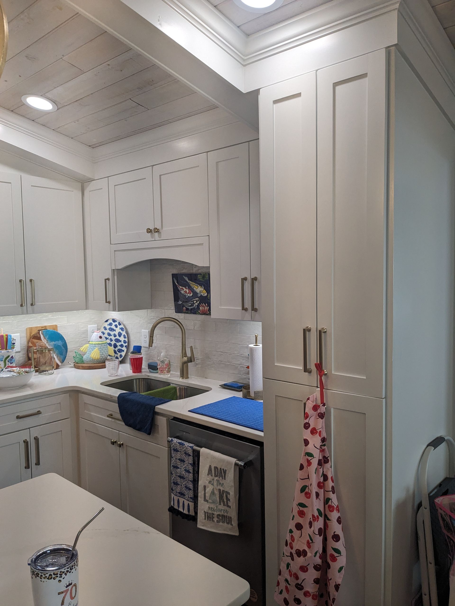 A light-colored kitchen with white shaker-style cabinets, a farmhouse sink, and a tall pantry closet with a patterned apron.