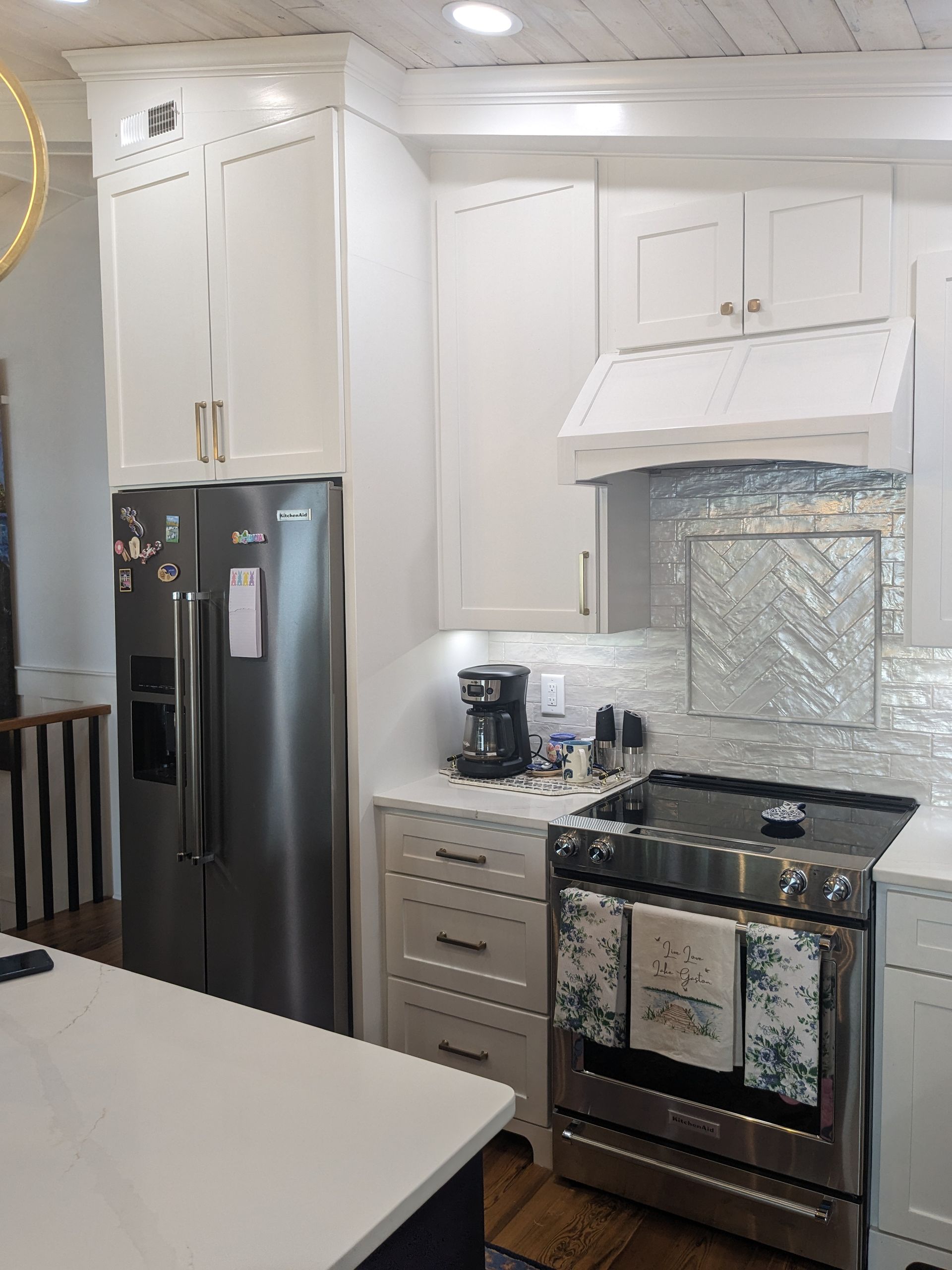 A bright kitchen with white cabinets, stainless steel appliances, and a grey herringbone tile backsplash.