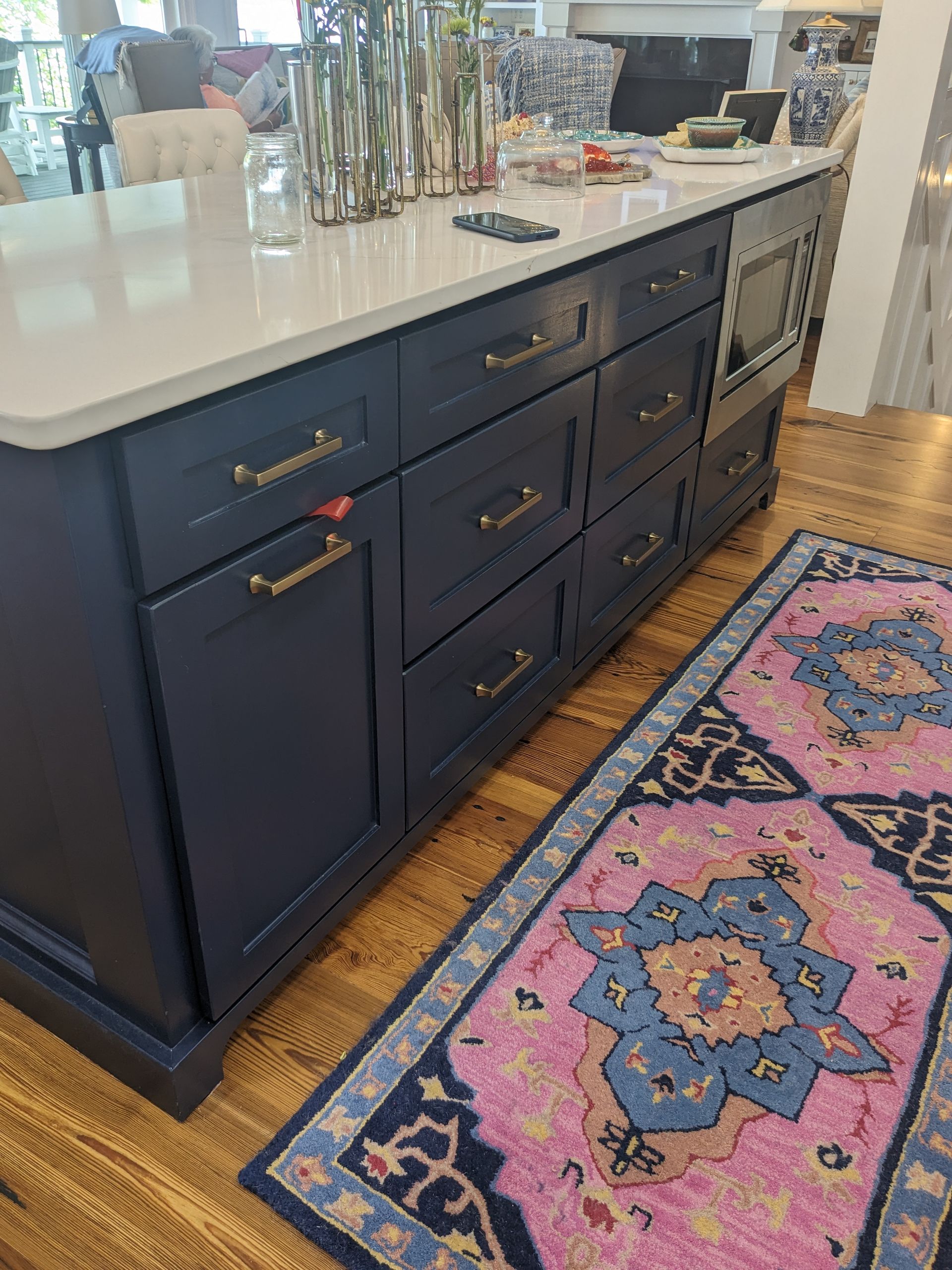 A navy blue kitchen island with gold hardware and a white countertop, next to a pink and blue patterned runner rug.