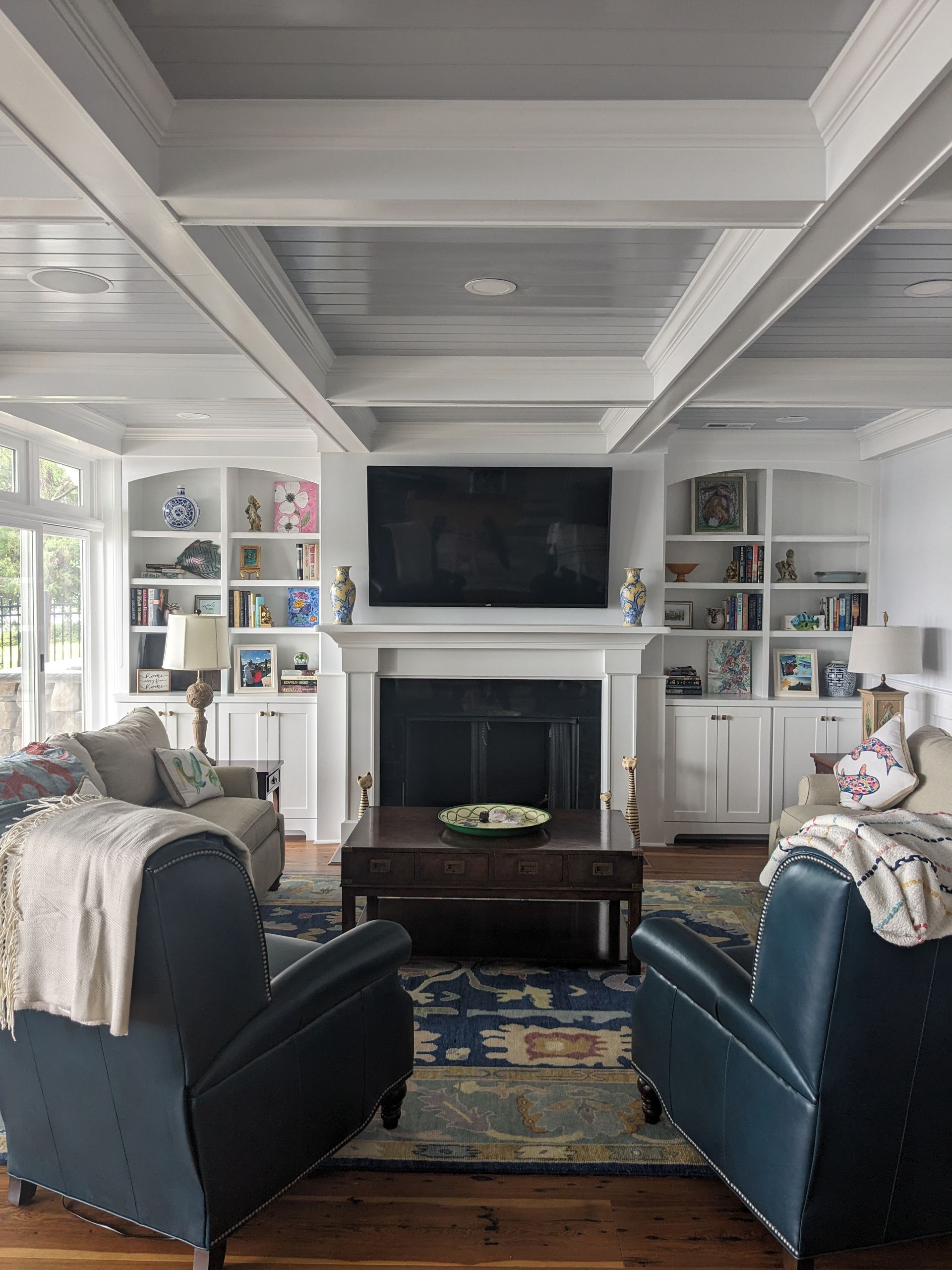 A living room with two dark blue armchairs facing a fireplace, a television, and white built-in bookshelves on both sides.