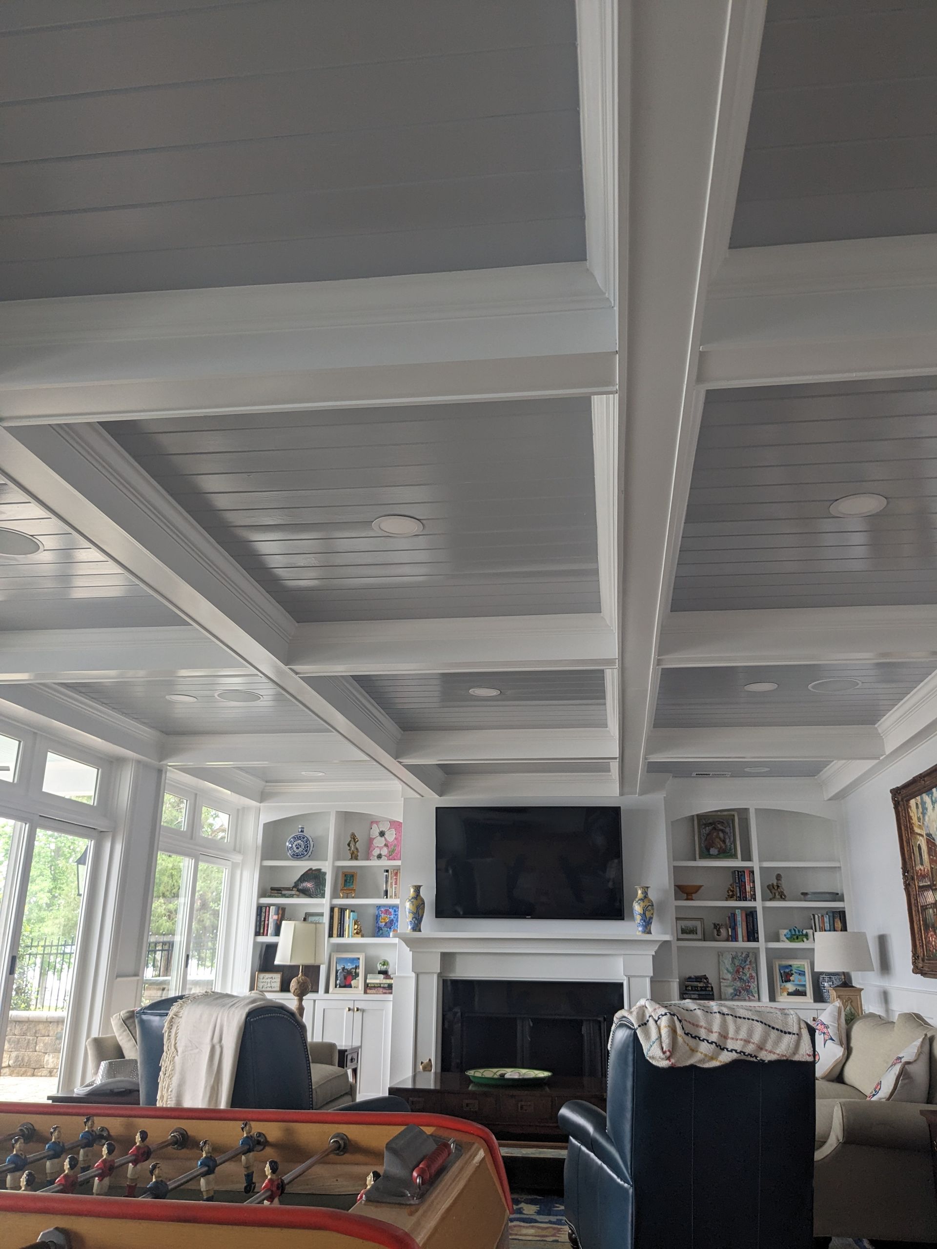 A cozy living room with a coffered ceiling, a fireplace with a mounted TV, and built-in white bookshelves on both sides.