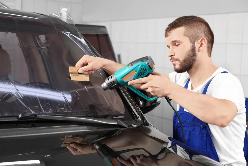 a Man is Applying Tinted Glass to a Car Windshield — Total Tint Bendigo in East Bendigo, VIC