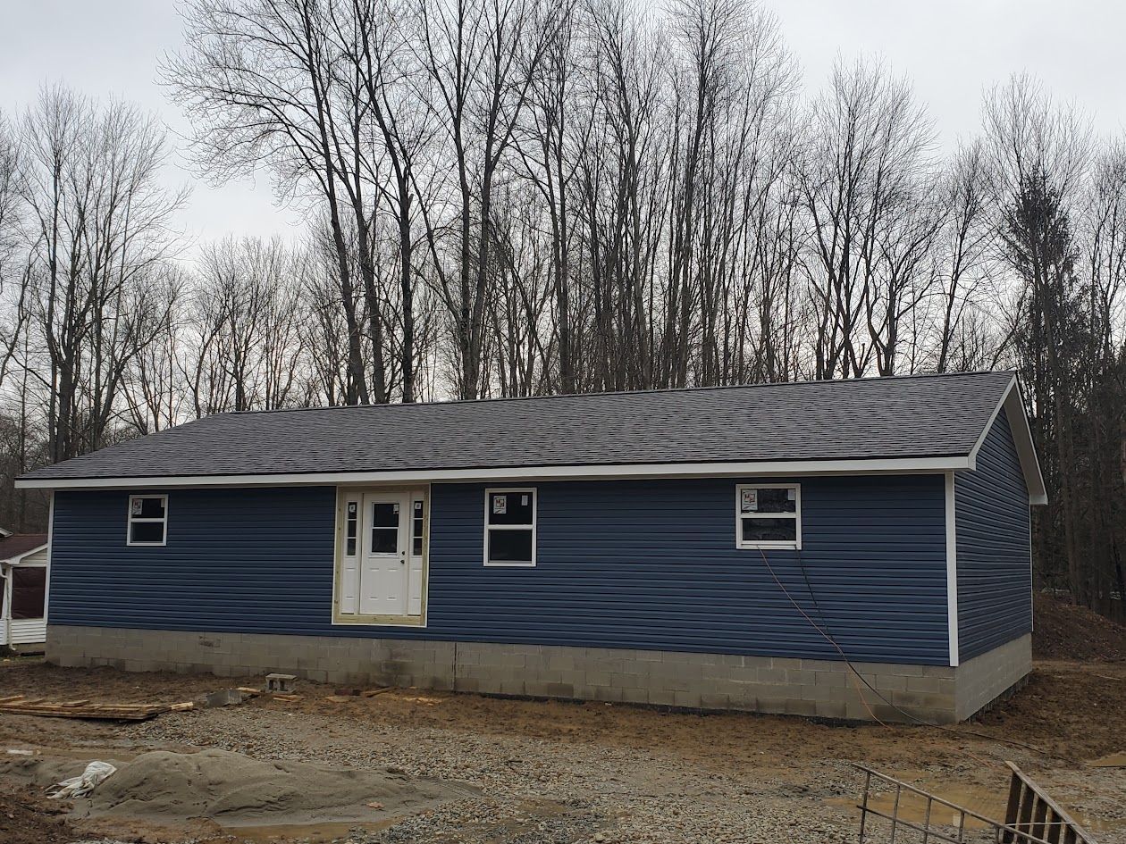 A blue house with a white door and windows is surrounded by trees.