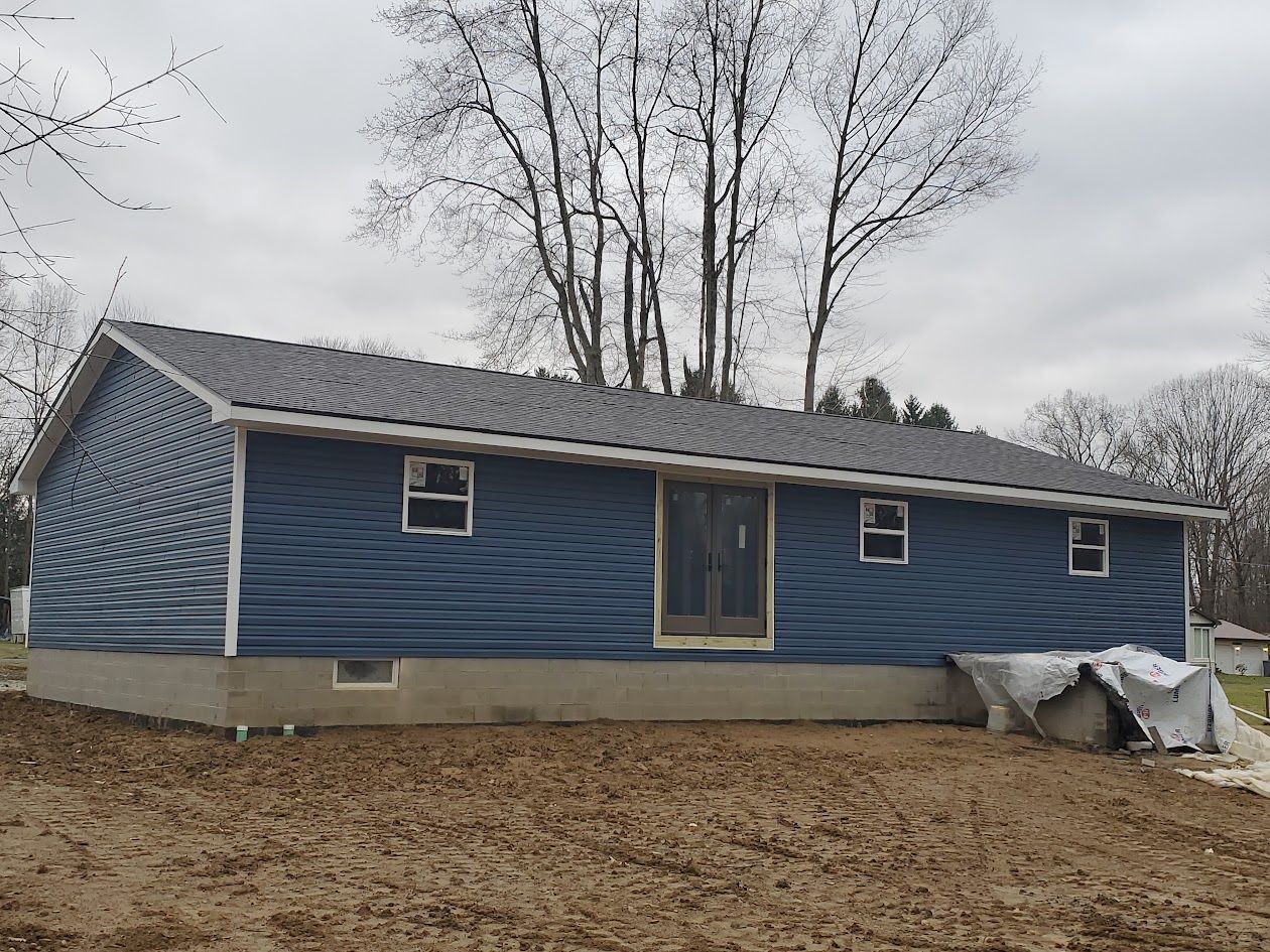 A blue house is sitting in the middle of a dirt field.