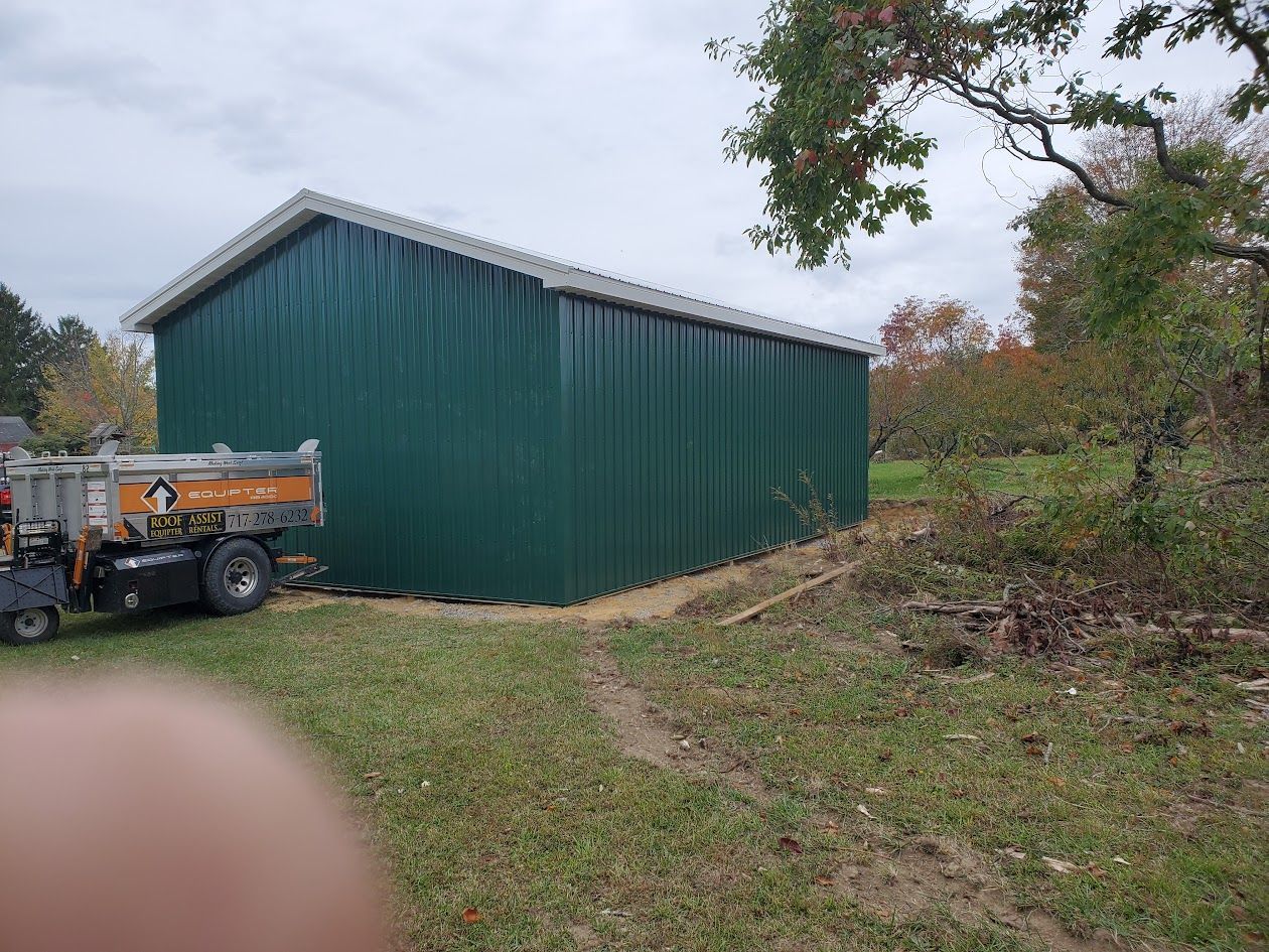A green metal building with a dumpster parked in front of it.