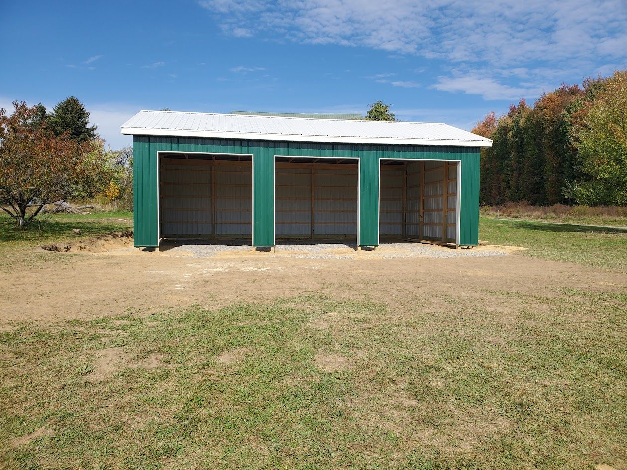 A green barn is sitting in the middle of a grassy field.