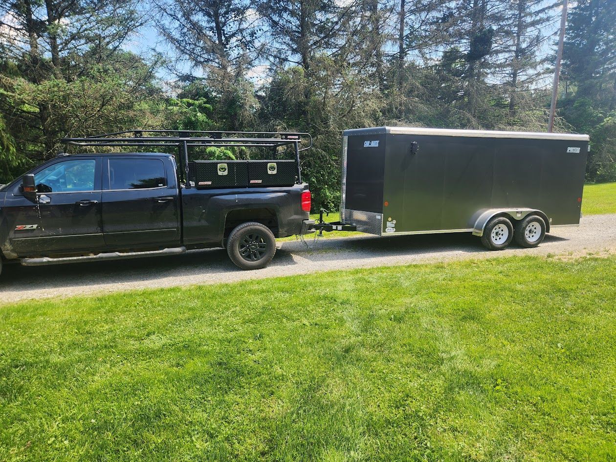 A black truck is towing a trailer down a dirt road.