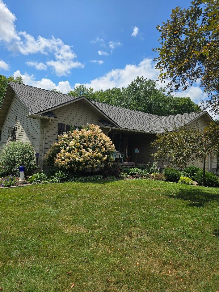 A house with a gray roof and a large lawn in front of it.