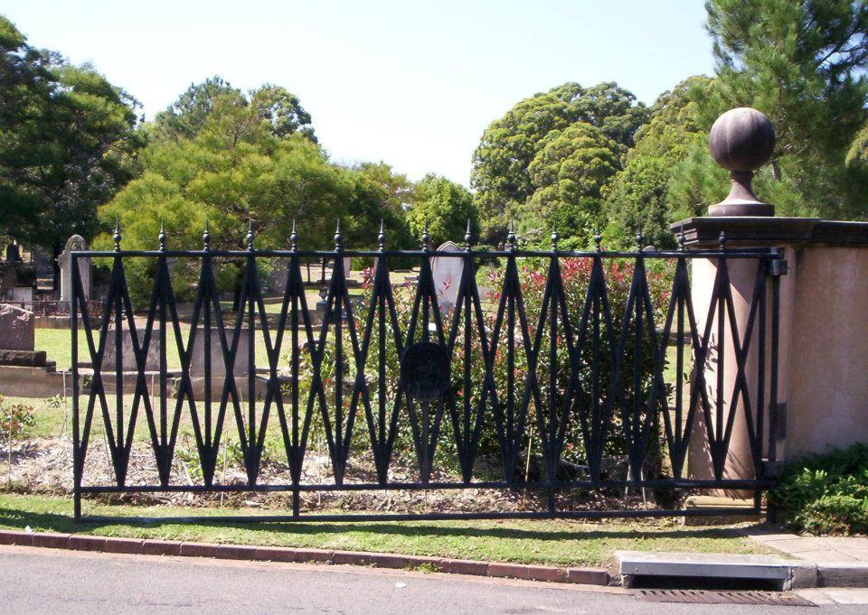 A wrought iron gate leading to a cemetery with trees in the background