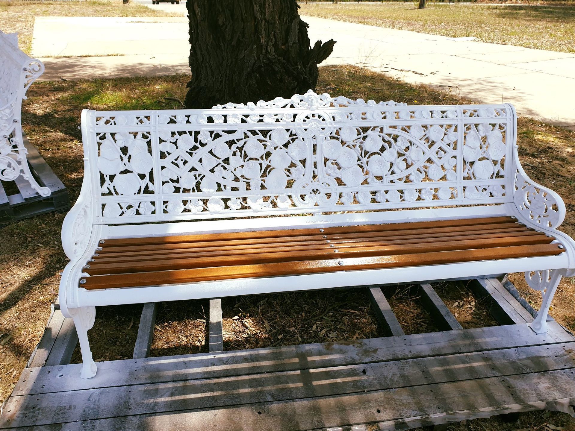 A white bench with a wooden seat sits on a wooden pallet