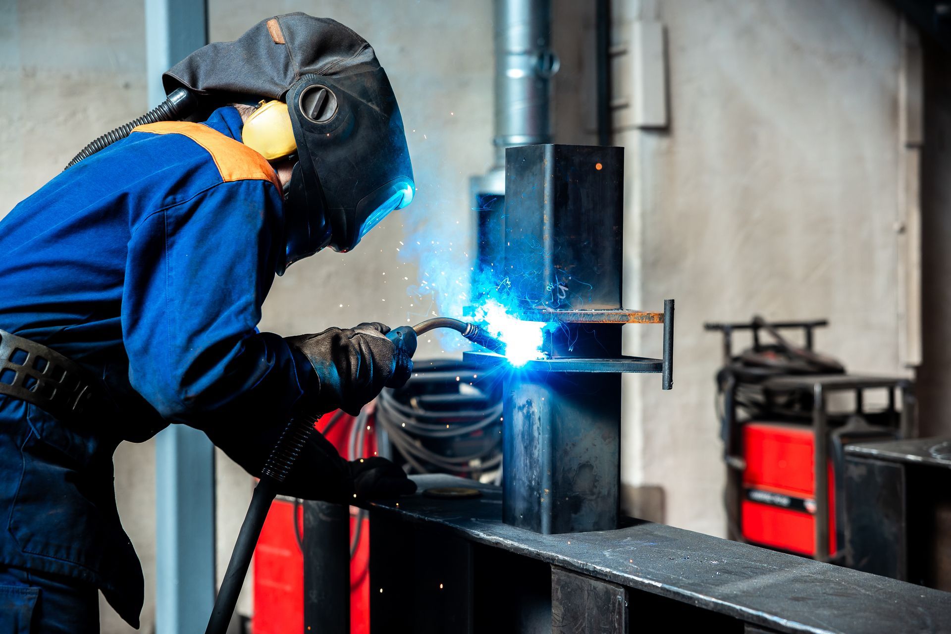 A skilful metal worker working with an arc welding machine while wearing safety equipment.