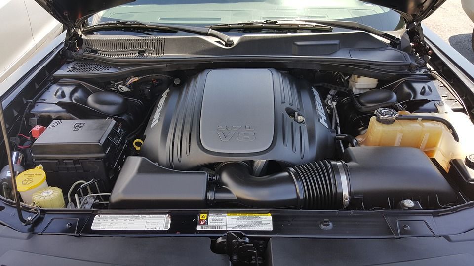 Black car engine bay with engine cover, air intake, and fluid reservoirs.