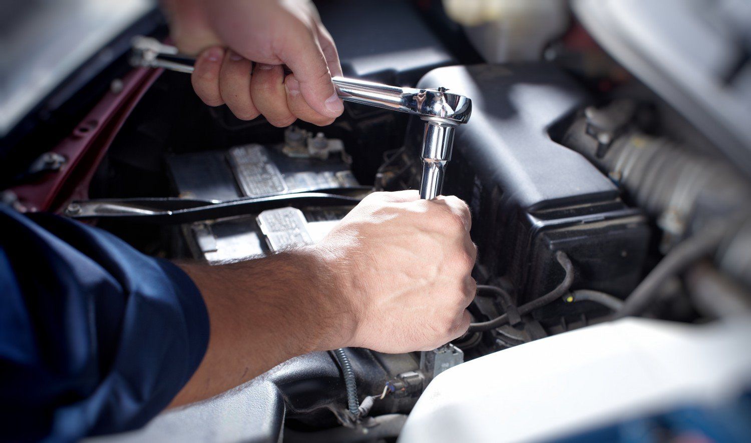 Hands using a wrench to work on a car engine.