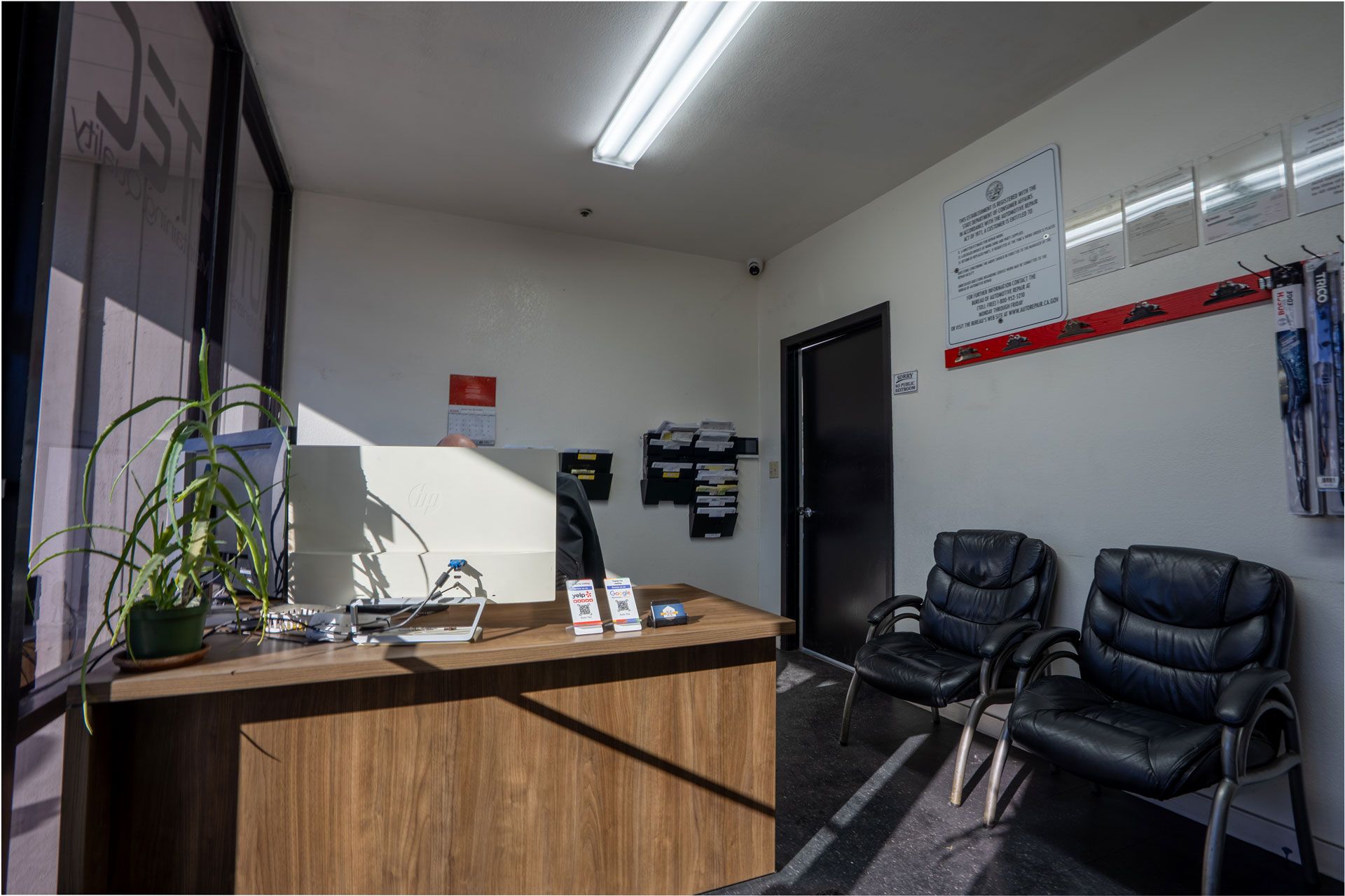 Reception area with a wooden desk, two black chairs, and a black door.