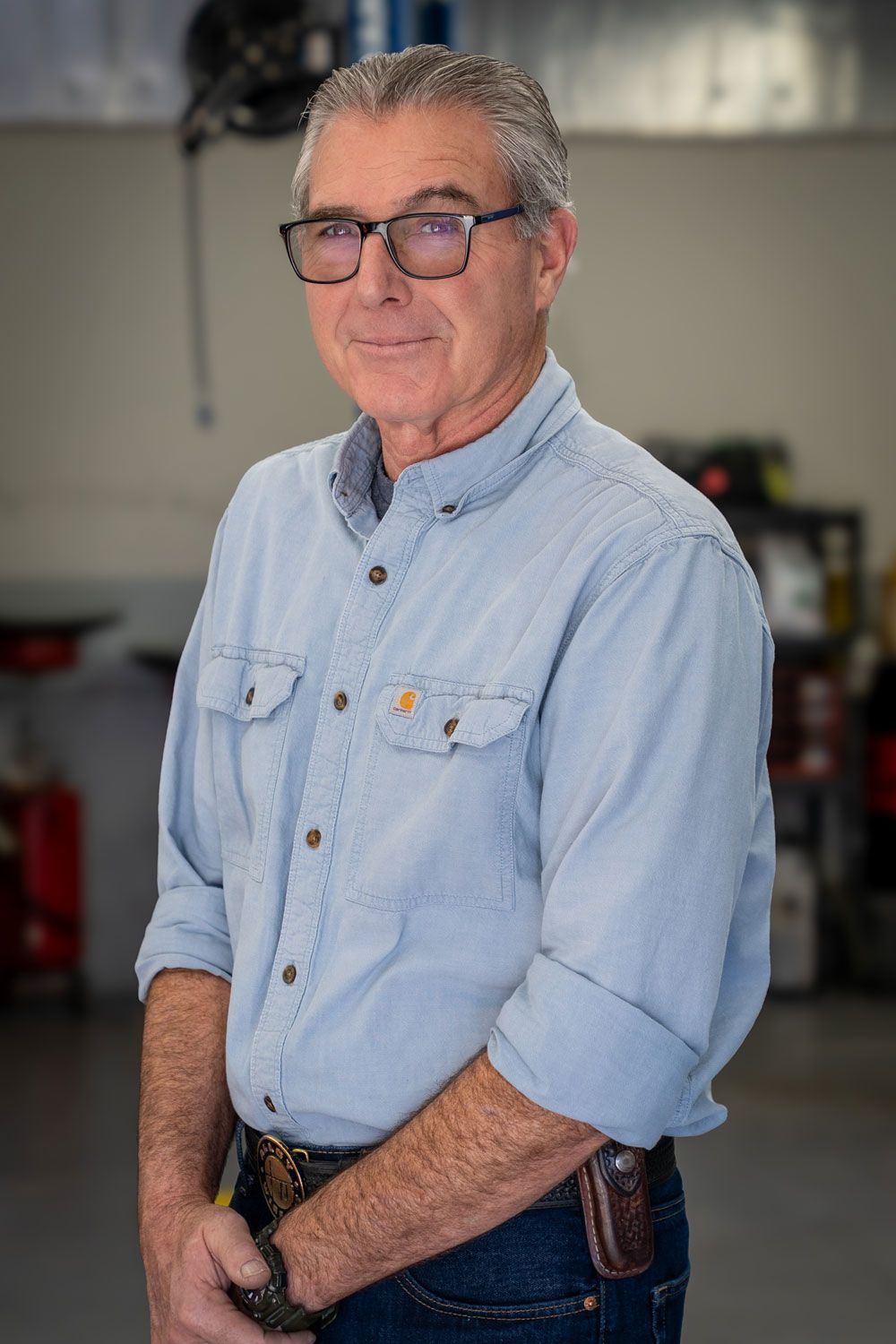Man in blue shirt and glasses, standing inside a garage.