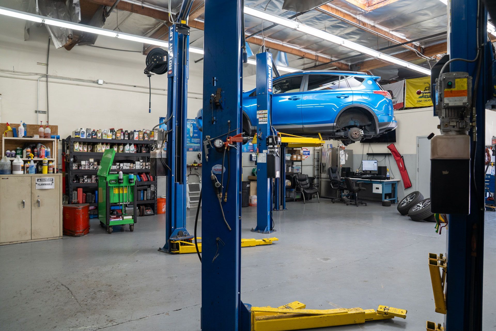 Blue car raised on a lift in a repair shop, tools and equipment visible.