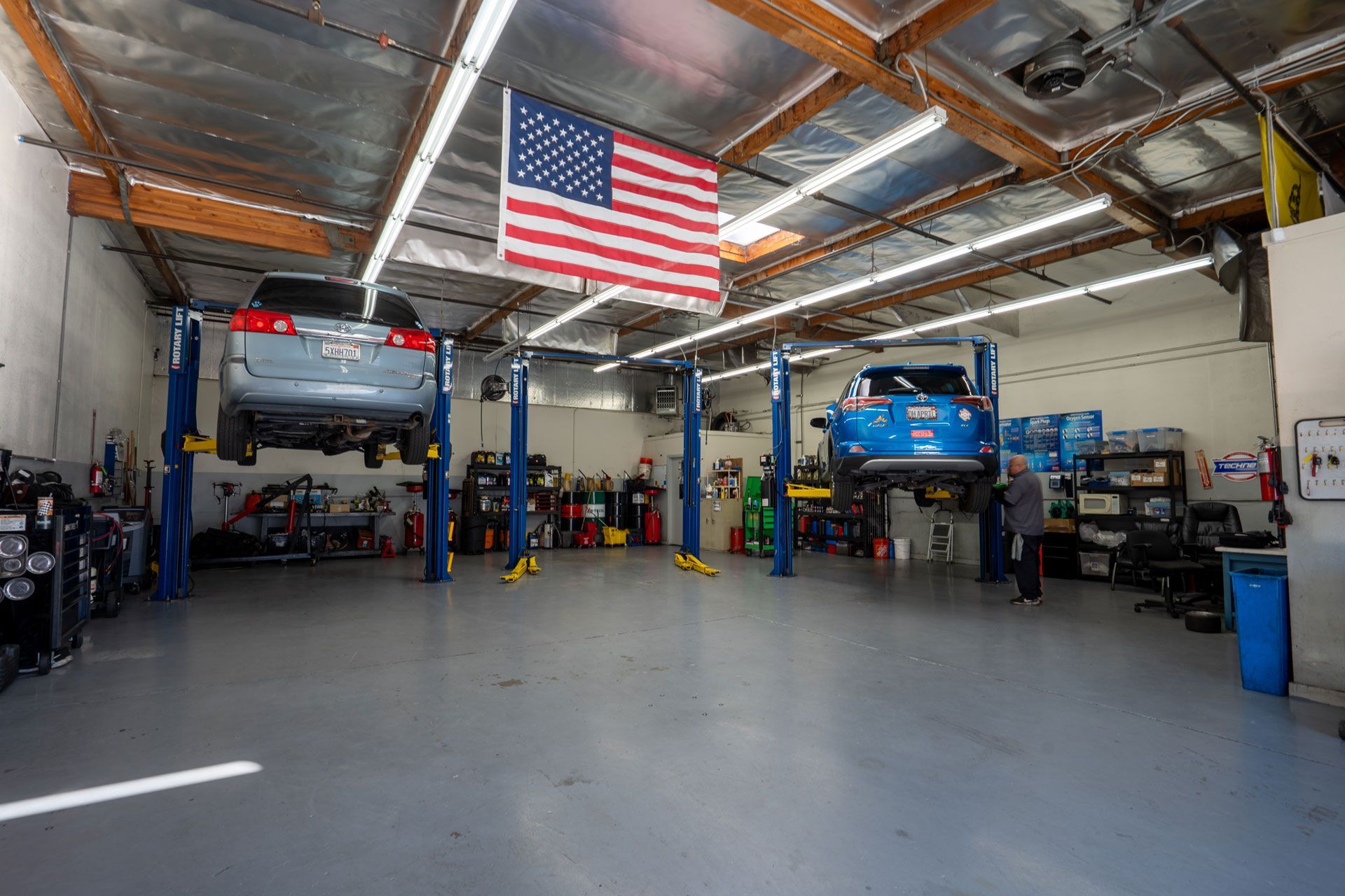 Auto repair shop with two cars raised on lifts, American flag hanging.