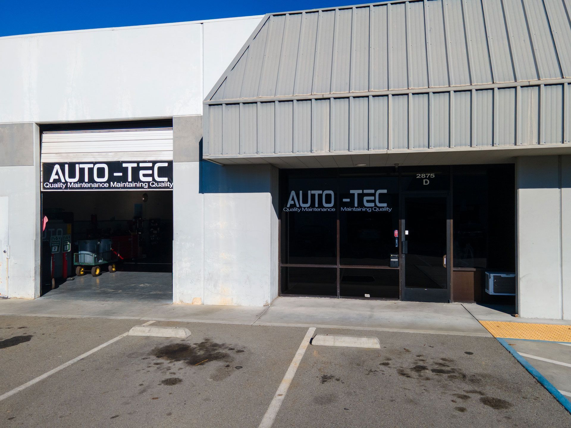 Exterior of AUTO-TEC auto repair shop with garage door open, showing the inside.