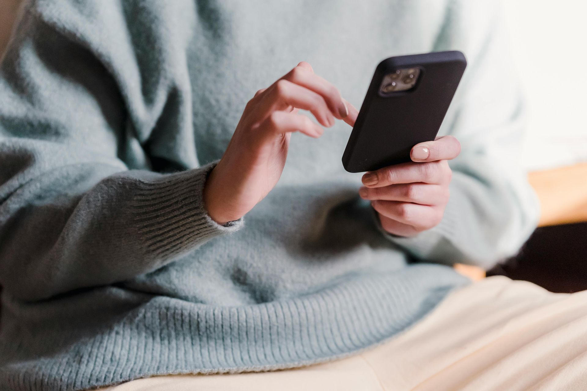 Person in light blue sweater using a black smartphone with right index finger.