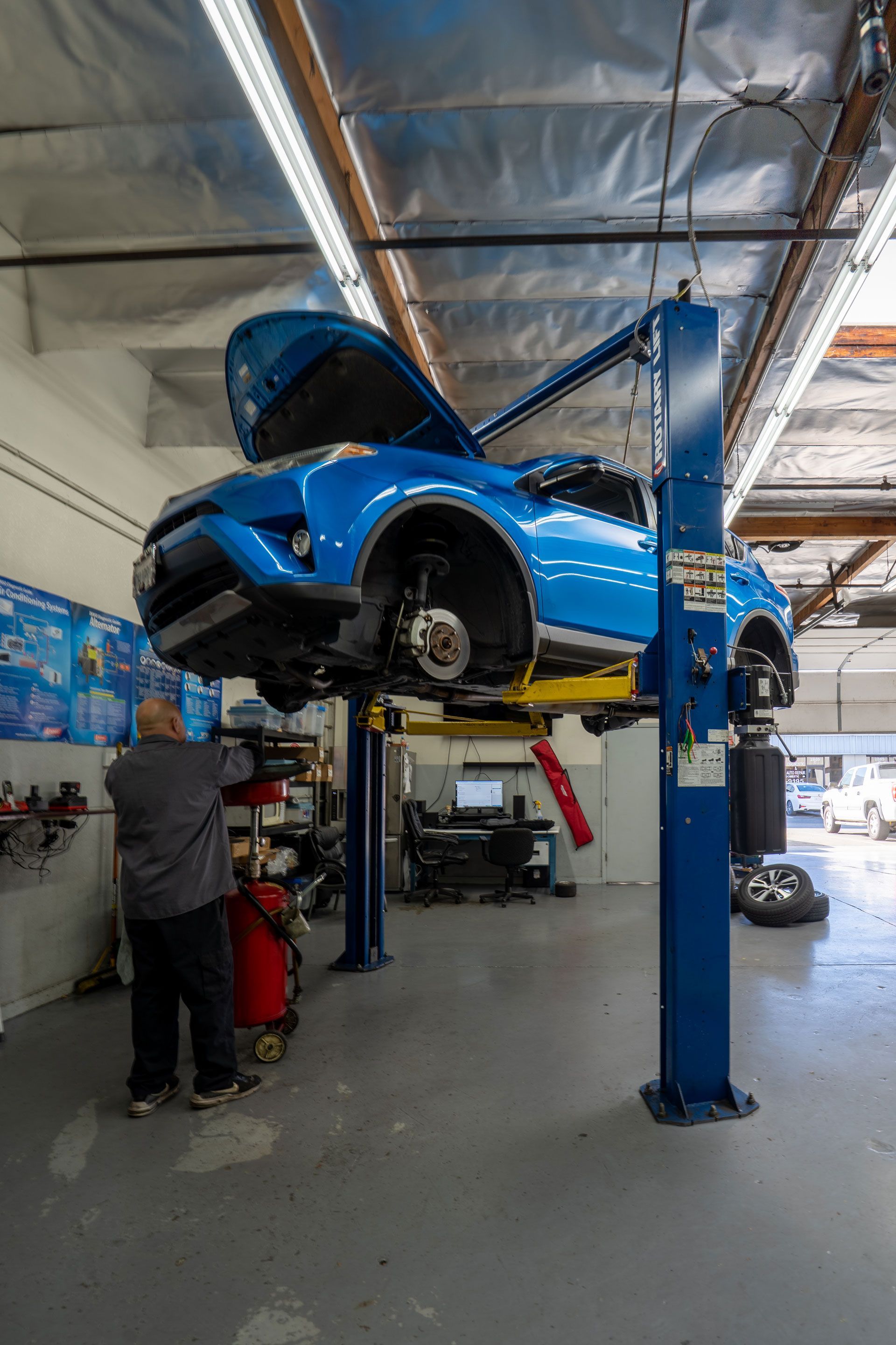 Blue car raised on a lift in a repair shop. Mechanic working near the car.