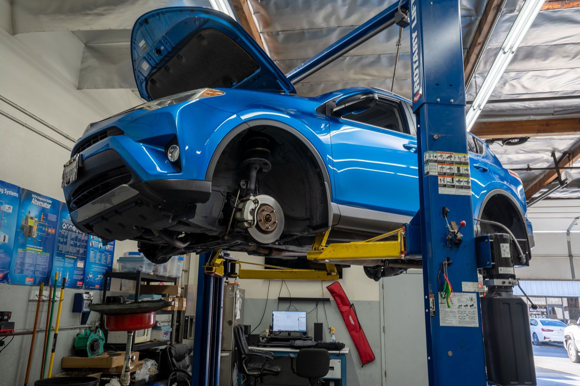 Mechanic in blue jumpsuit using diagnostic tool on a car in a garage.