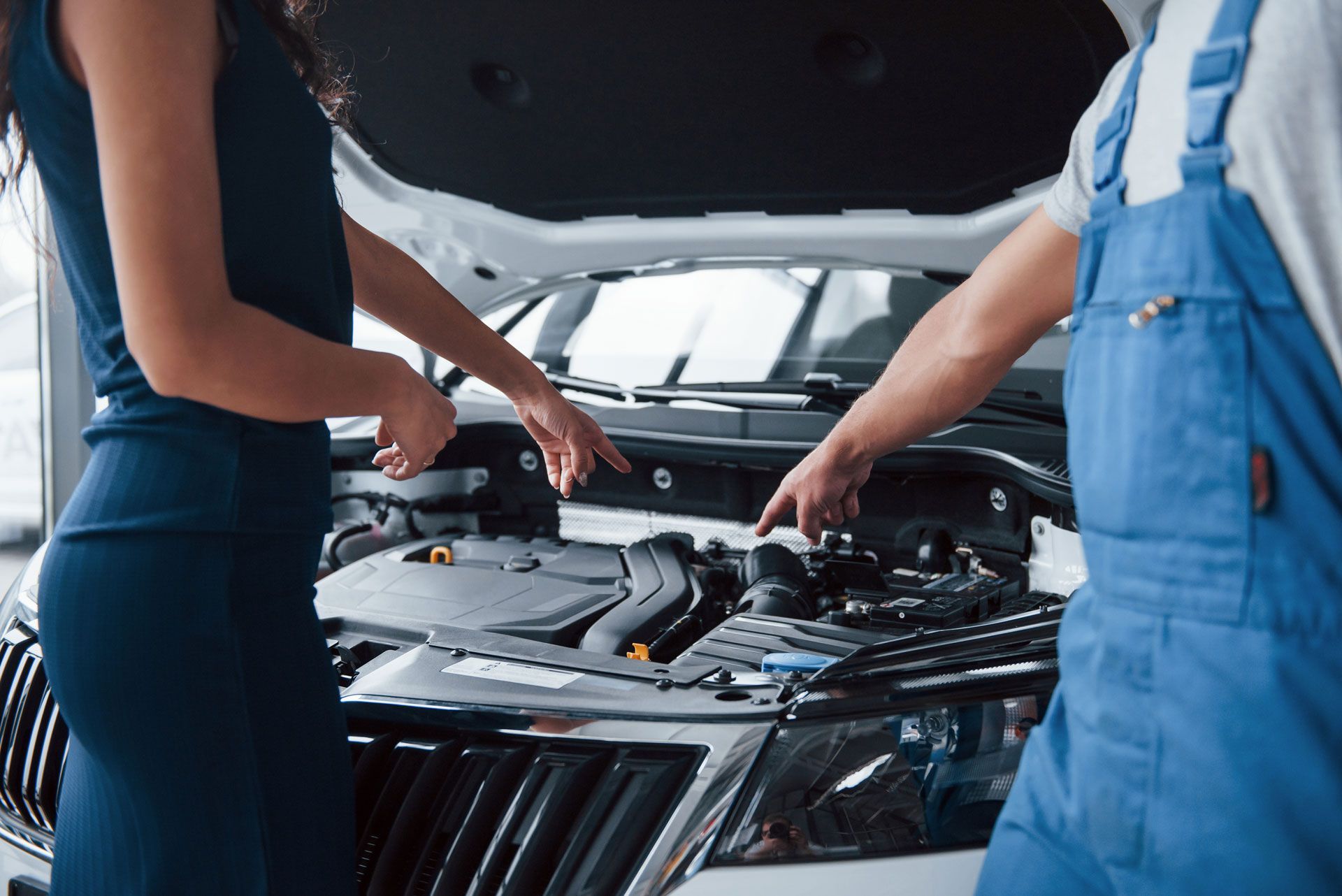 Woman and mechanic pointing at car engine in open hood.