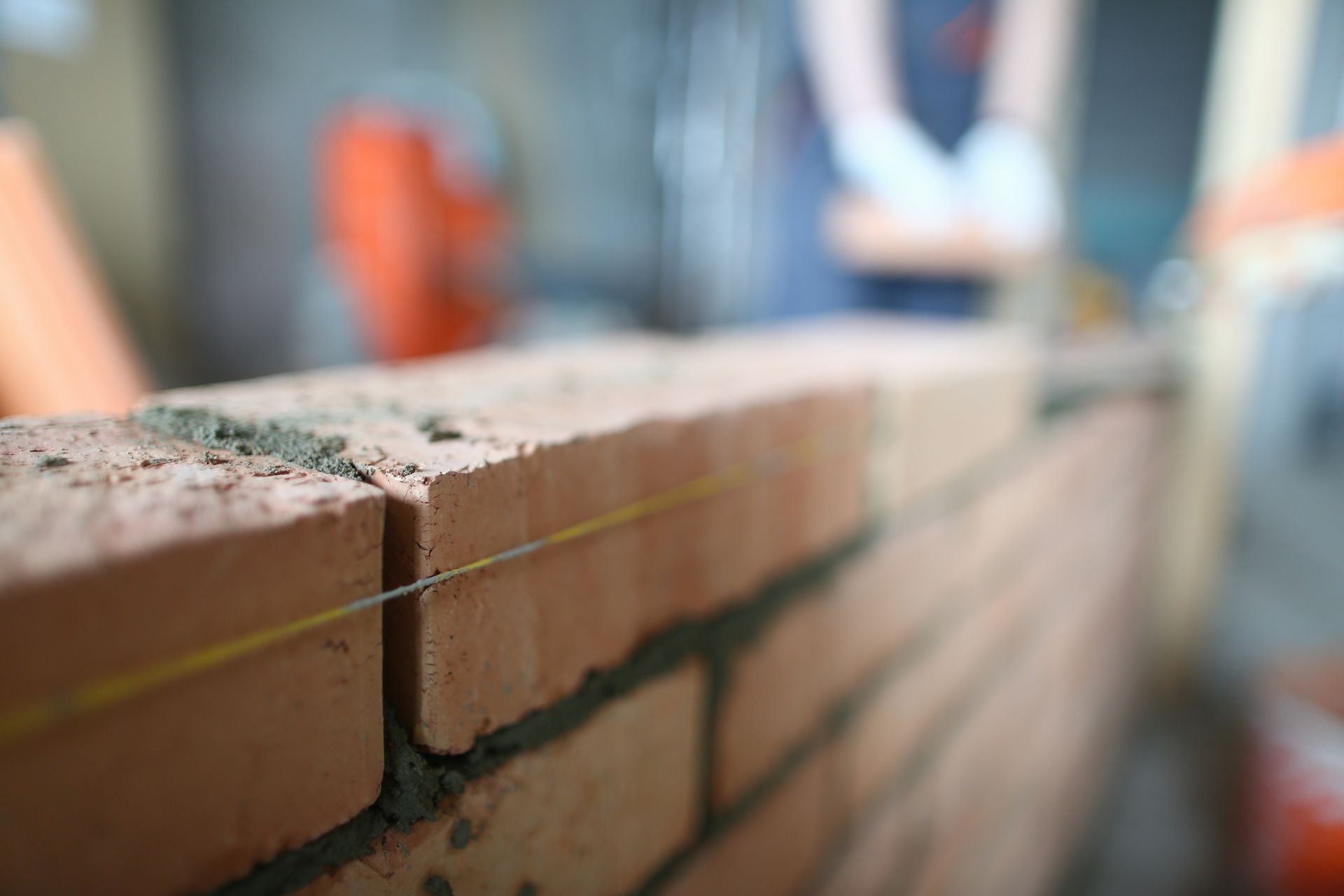 Close-up of a brick wall under construction with a guide line stretched across the top.