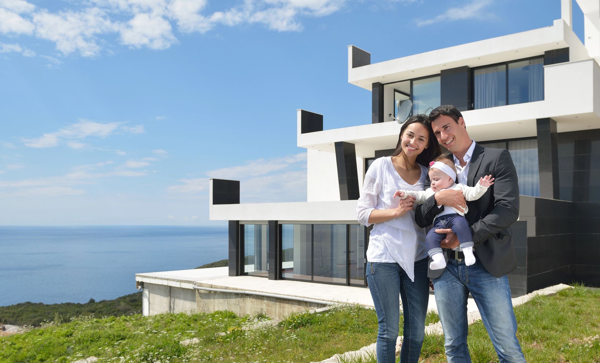 A family is standing in front of a modern house holding a baby.