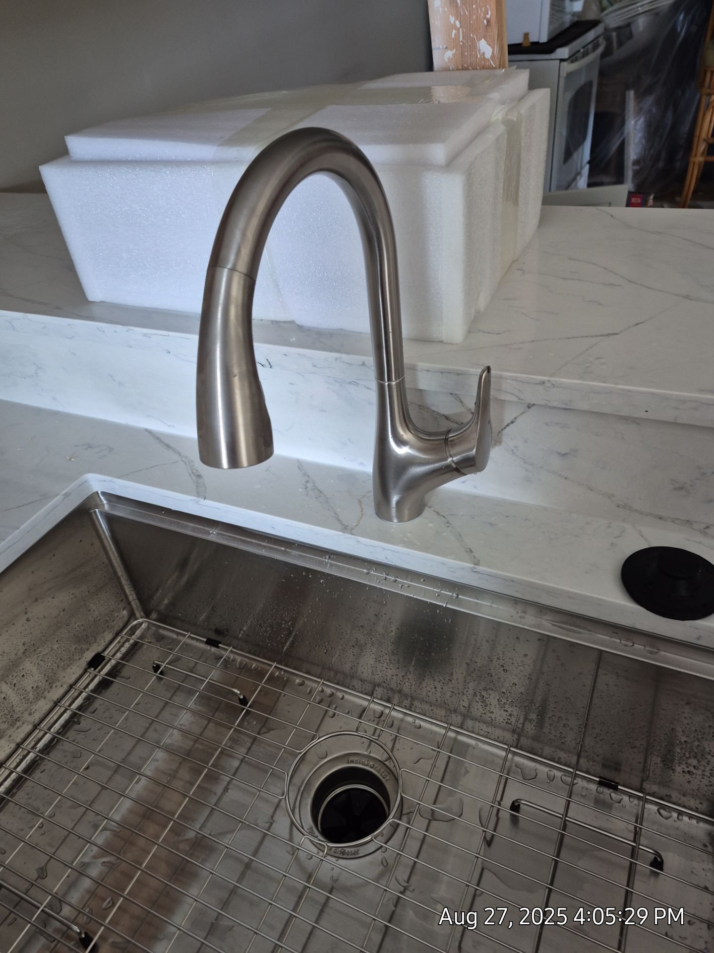 Brushed nickel kitchen faucet over a stainless steel sink, set in a white countertop.