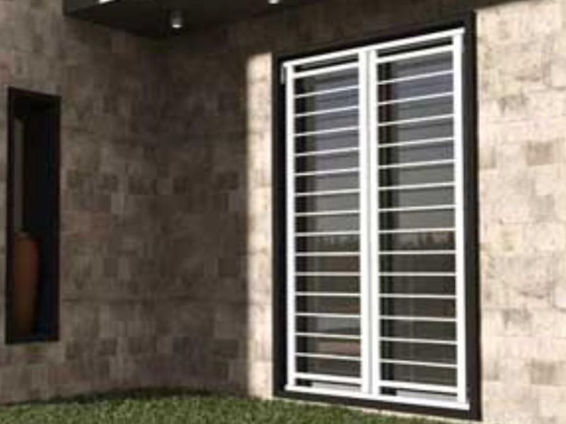 Una finestra con una griglia di metallo si trova su un muro di mattoni.