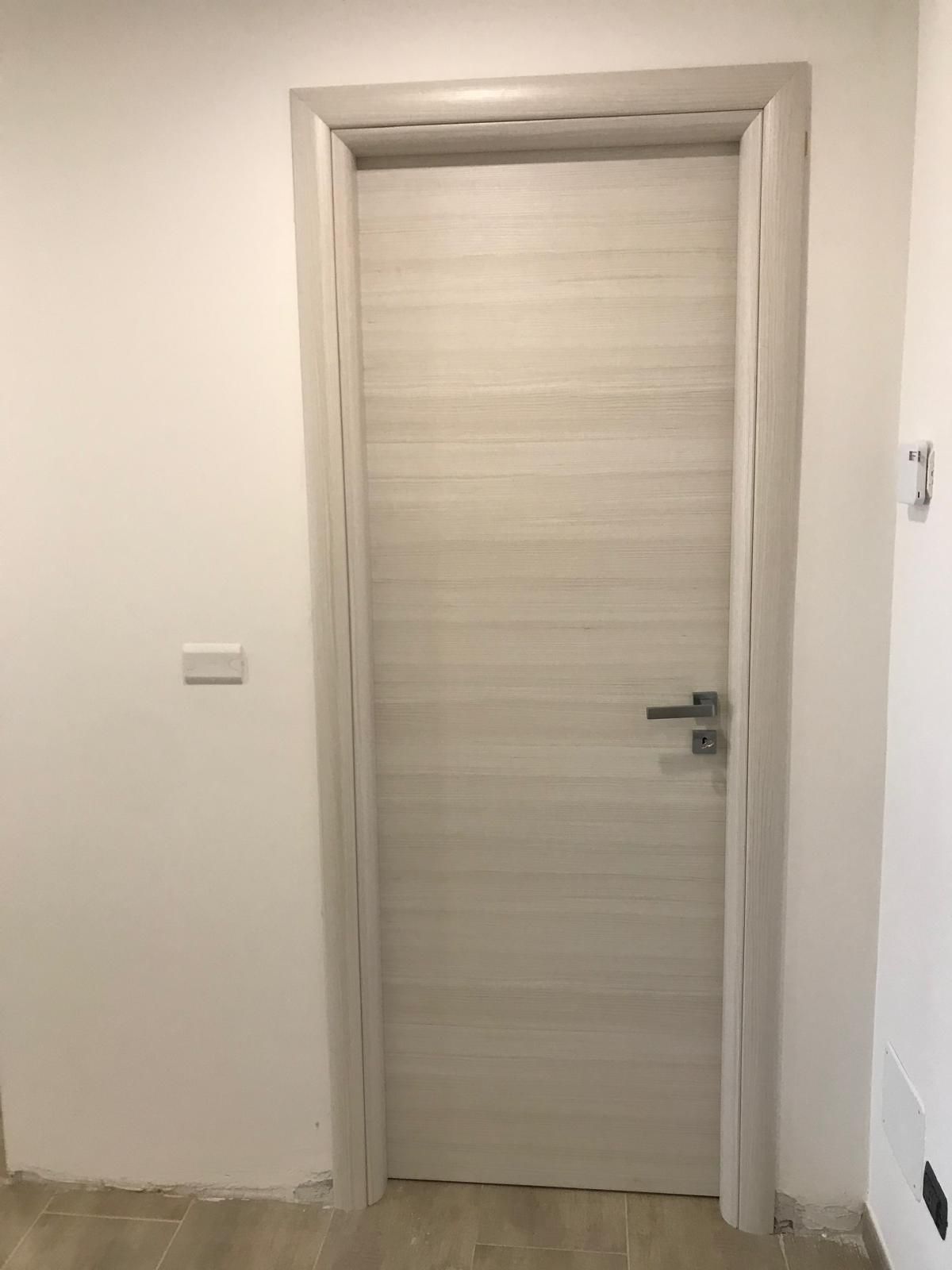 Una porta bianca si trova in un corridoio accanto a un muro bianco.