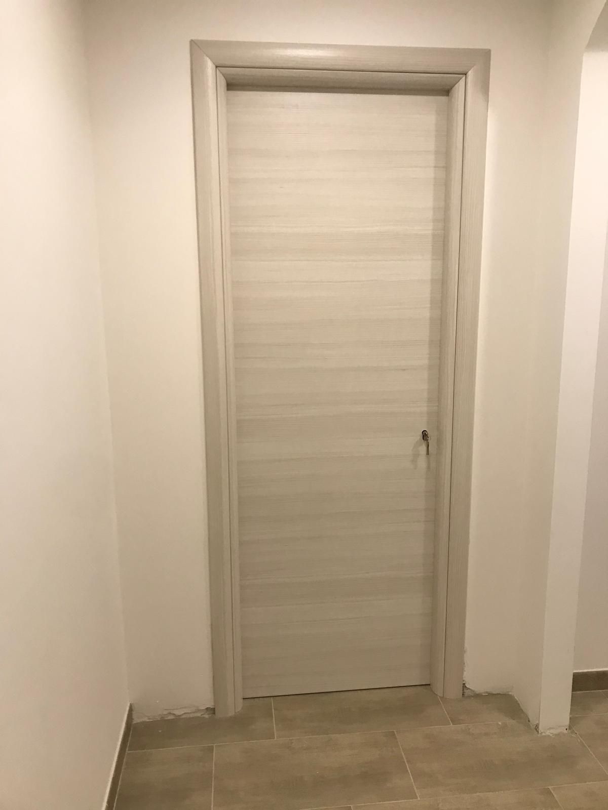 Una porta bianca si trova in un corridoio accanto a un muro bianco.